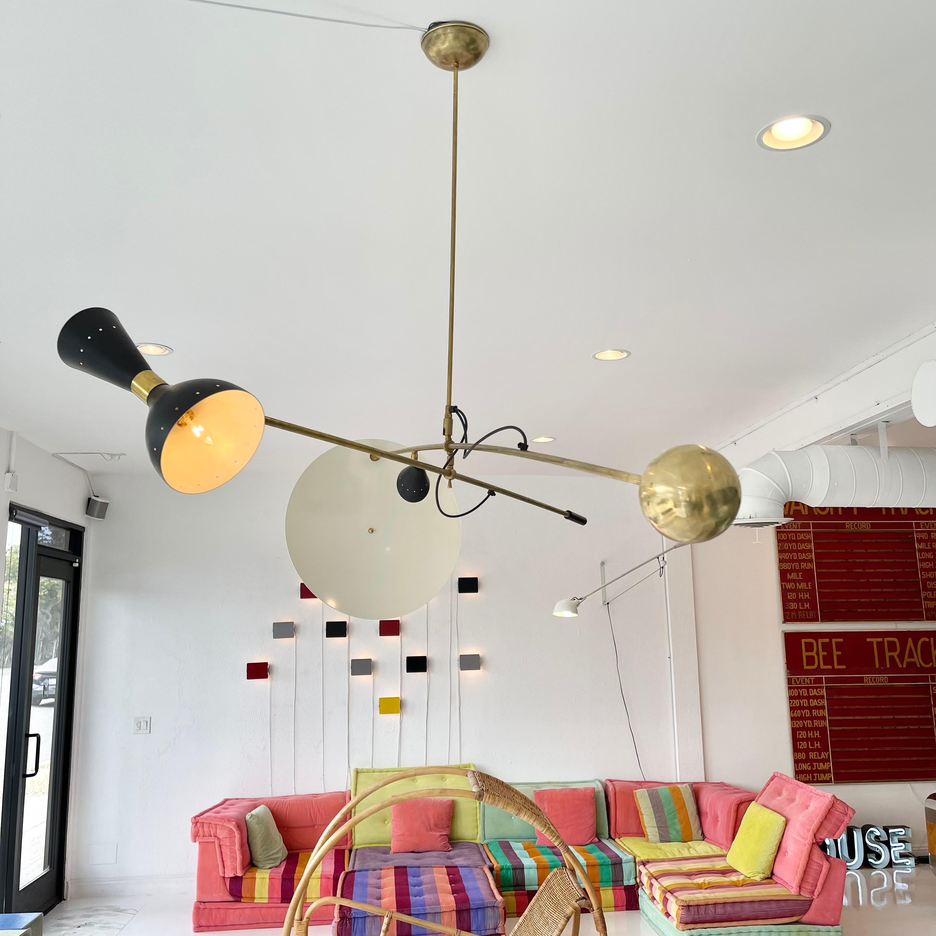 Large architectural chandelier in the style of Stilnovo. Chandelier has two large brass arms that can swing in multiple directions. One arm features a large brass ball counterweight on one end, and on the other, a perforated metal cone which shines
