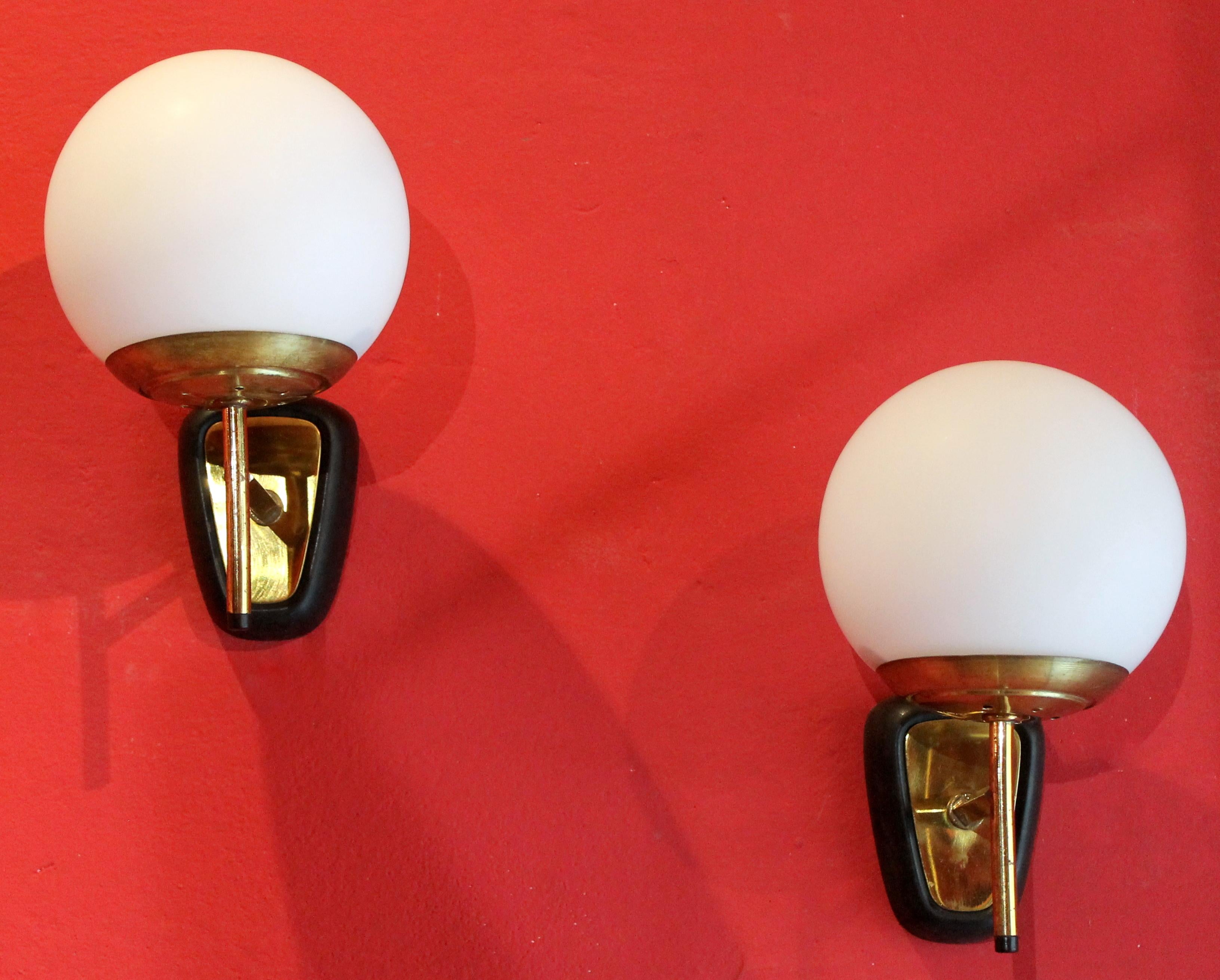 This pair of Mid-Century Modern Italian design modernist wall light in the style of Stilnovo has one gilt brass arm holding a glass ball shaped shades resting on round concave gilt brass bobeche.
Each gilt brass arm with black lacquered final is