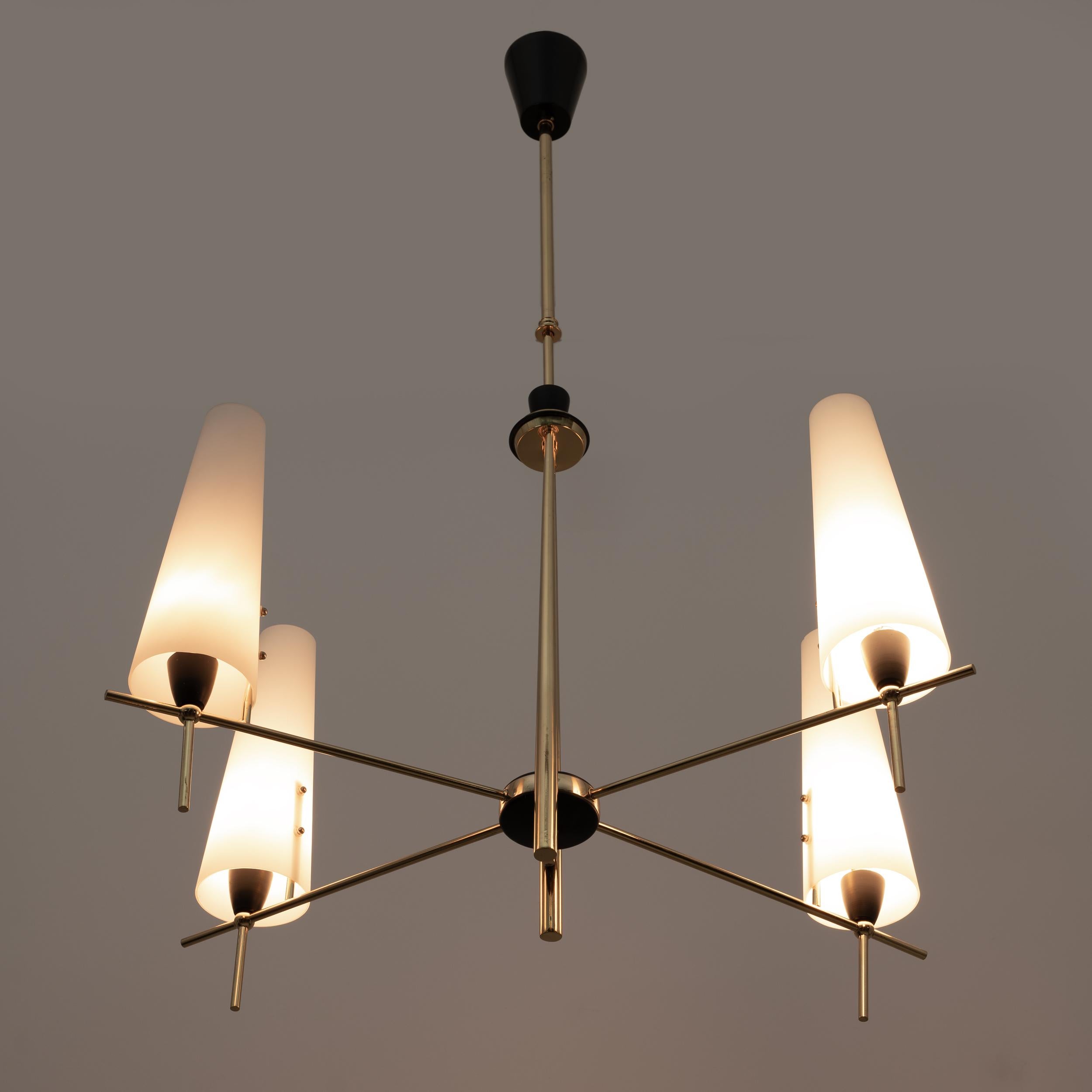 Mid-century chandelier, a polished brass stem with four arms supporting long, narrow globes of opaline white glass secured by brass pins. Each glass cone is equipped with a candlestick socket. In the style of Stilnovo, but the manufacturer's marks