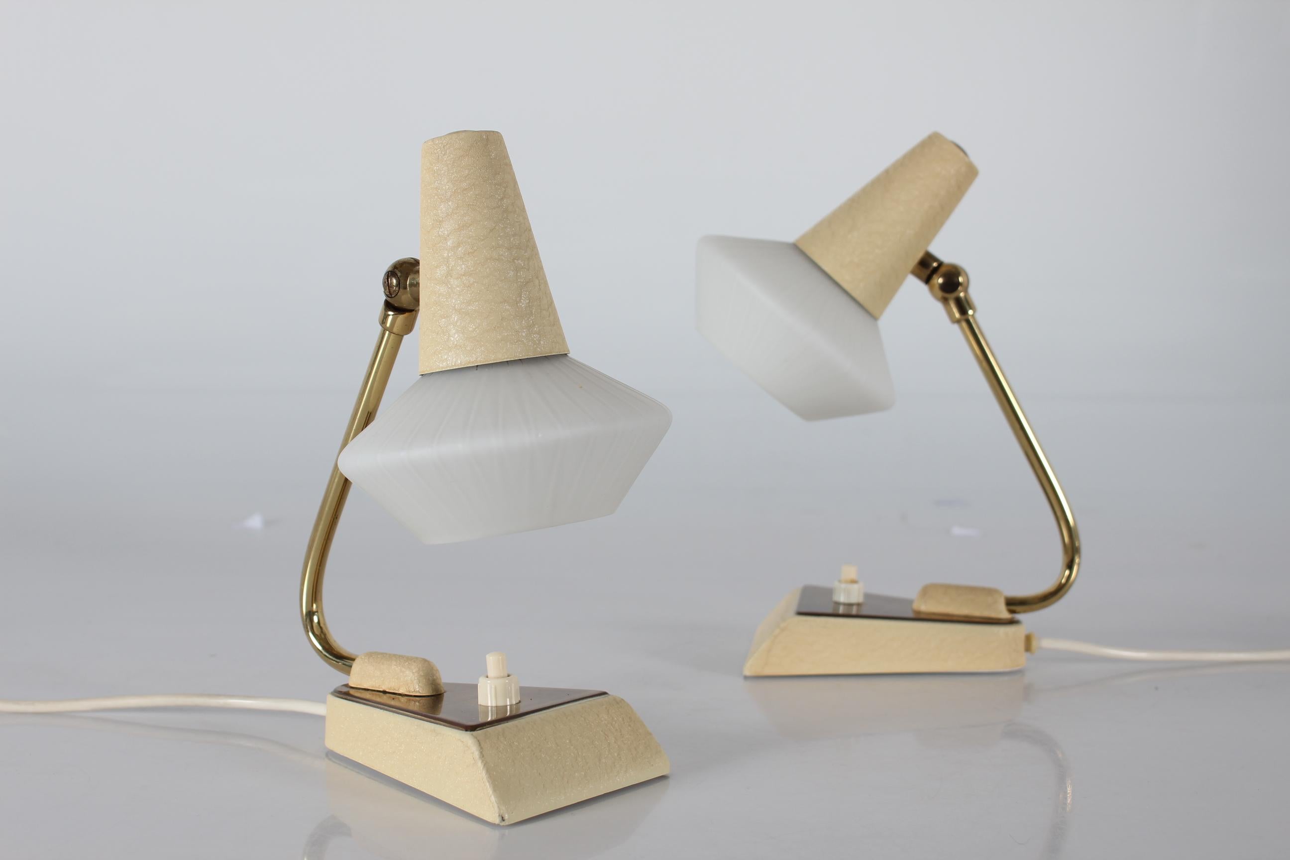 Pair of European probably German bedside table lamps in the style of Stilnovo.
The small lamps have a triangular base with brass lid and a built-in switch.
The metal parts have a slight embossed pattern with cream colored lacquer. The adjustable