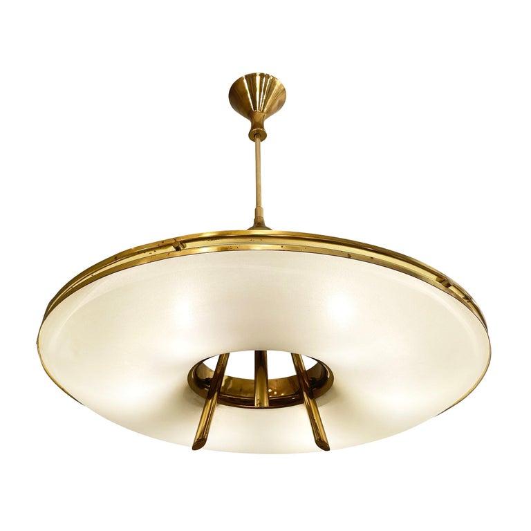 Saucer shaped chandelier by Stilnovo with two frosted glass shades on a brass frame. The architectural and well thought out design is highlighted by the three stems that merge into one and the contoured canopy. Holds six candelabra sockets. Height