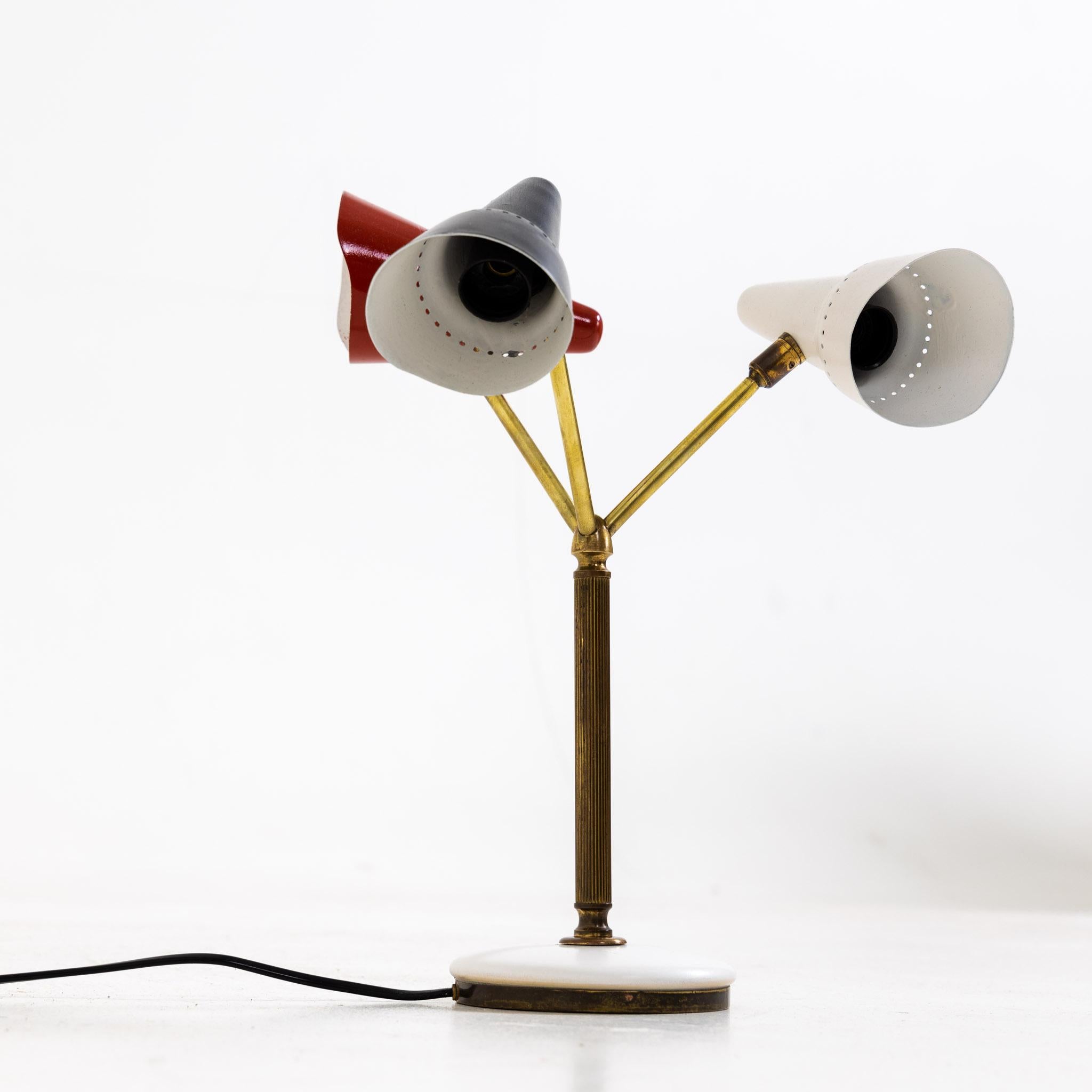 Small table lamp with brass stem and round marble base and three conical lampshades in black, red and white.