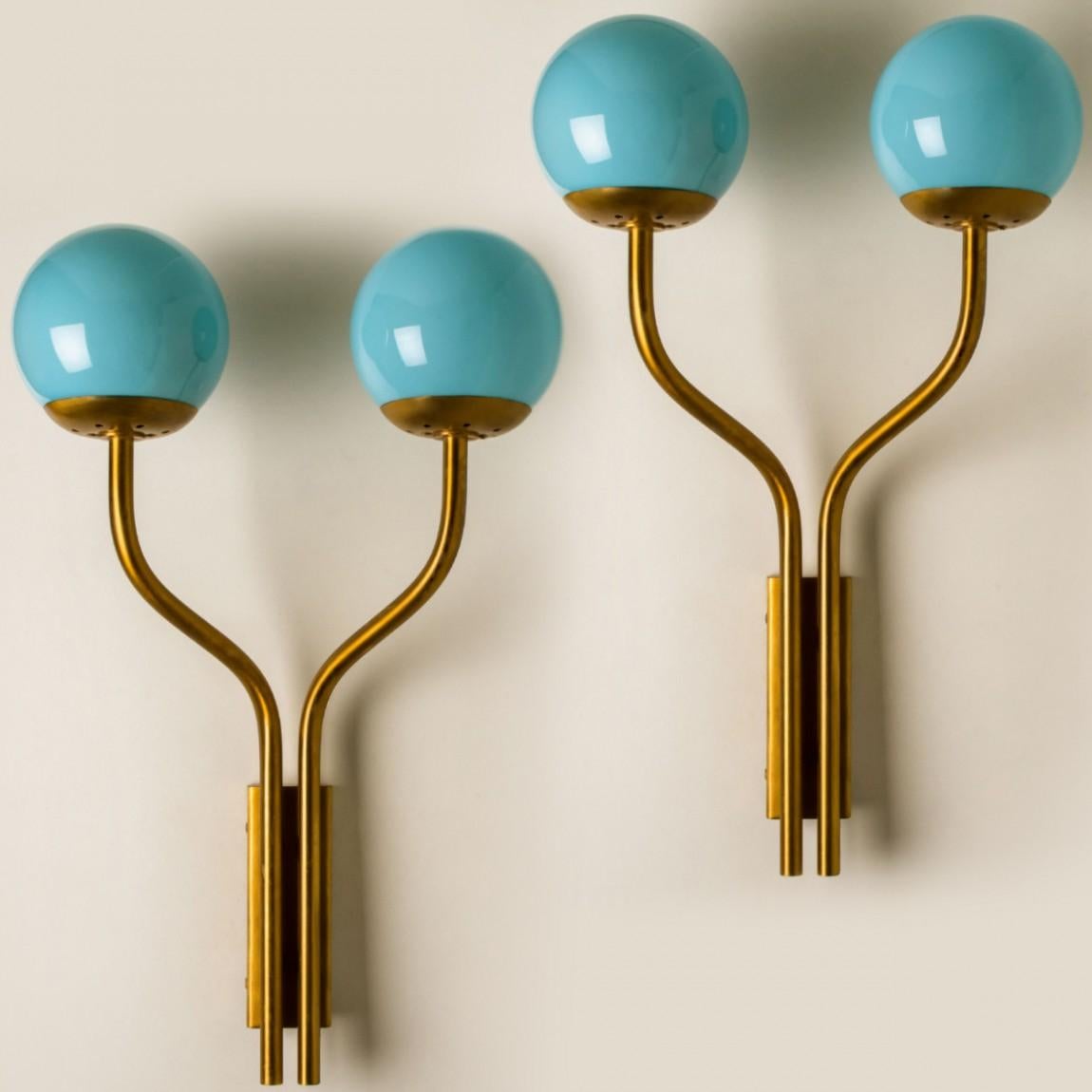 Playful blue wall lights, in the style of Stilnovo, made in Italy, around 1960. The wall lights are made of a brass frame with two arms holding a blue glass ball. When the lights are on, they give a warm light. As shown in the