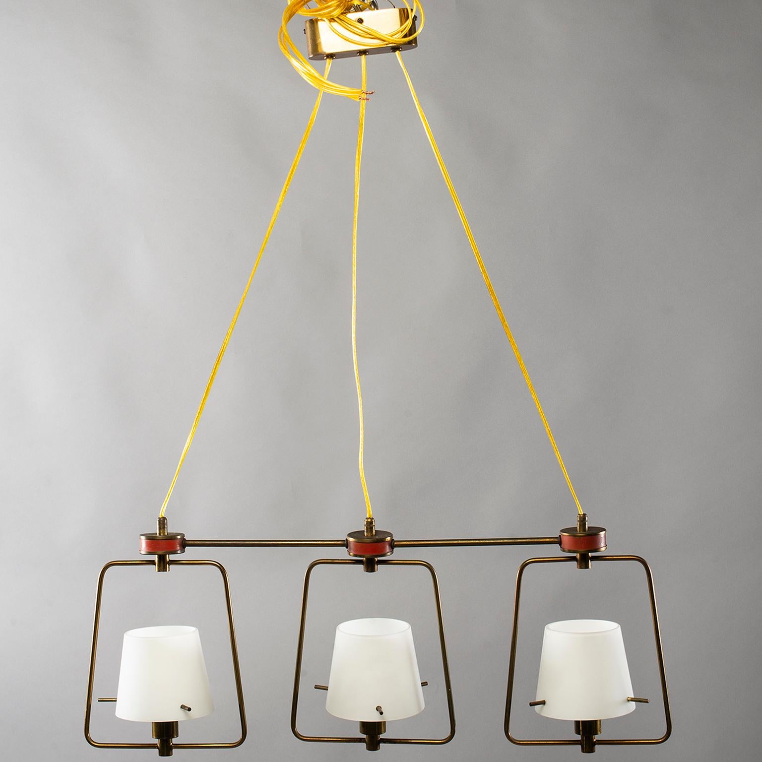 Stilnovo style Italian three light fixture, circa 1960. Brass tubing frame has red enamel accents and features adjustable length electrical cording and three glass shade lights with candelabra sockets. Glass shades are secured with brass pins.