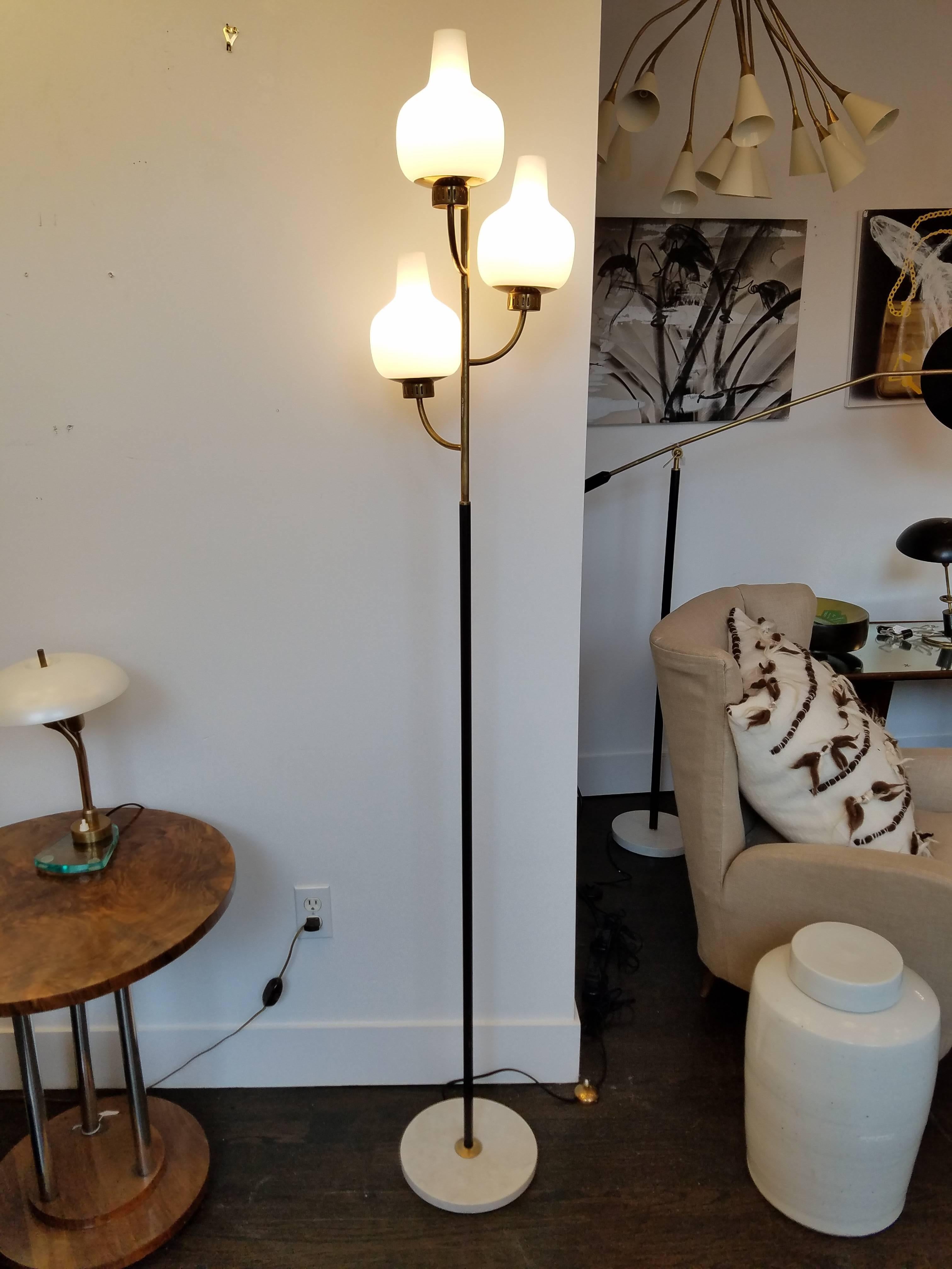 Vintage 1950s Italian floor lamp by Stilnovo, featuring three brass arch branches holding individual frosted white globes. Brass pole has black enamel lower part and is supported on a marble base. Made in Italy.