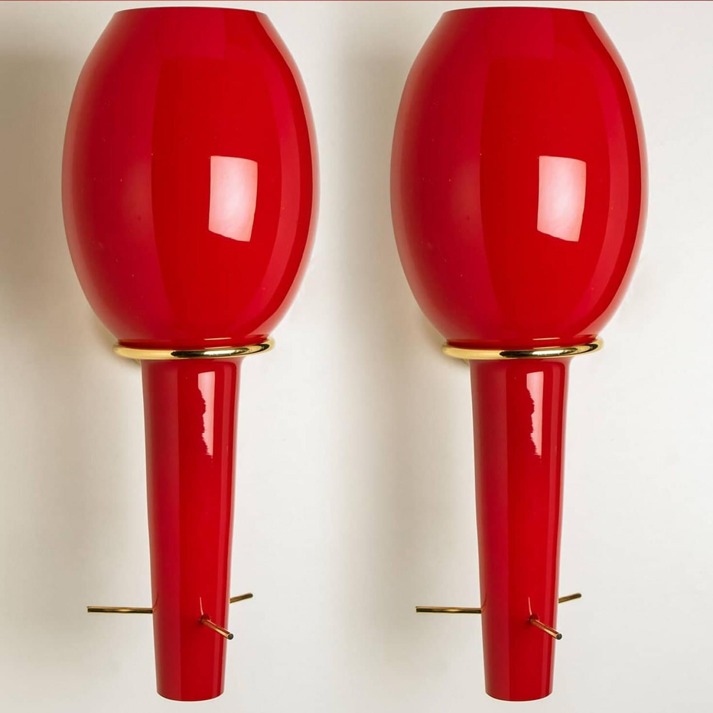 Luminose luci da parete rosse, realizzate da Stilnovo in Italia, Europa, intorno al 1960. Le applique sono costituite da una struttura in ottone che sostiene il vetro rosso. Quando le luci sono accese, emettono una luce rossa e calda. Come mostrato