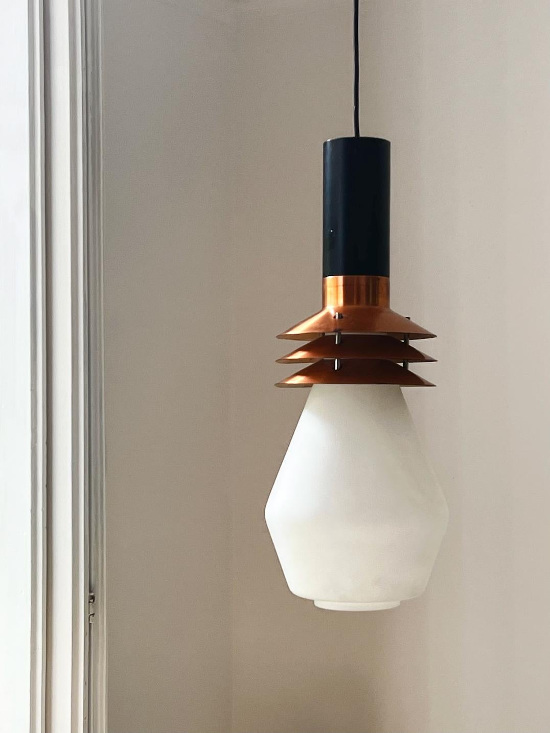 Large pendant light by Stilnovo of Italy. Mid-20th century. Stilnovo label.

The fixture comprises a large white glass shade with an opaque satin finish below a tiered copper diffuser, completed by a black metal tube. The yellow Stilnovo label -