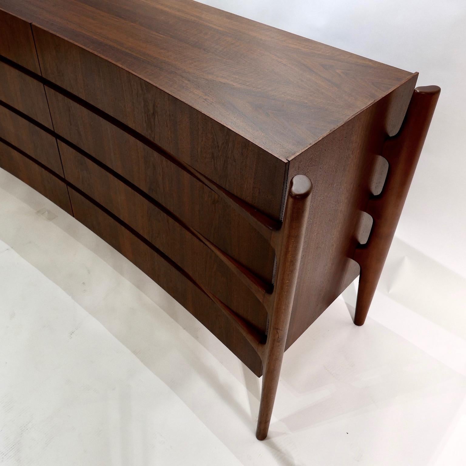 Exposed carved walnut legs with a curved bookmatched walnut front. Beautiful and sculptural eight drawer dresser designed by William Hinn for Urban Furniture's 