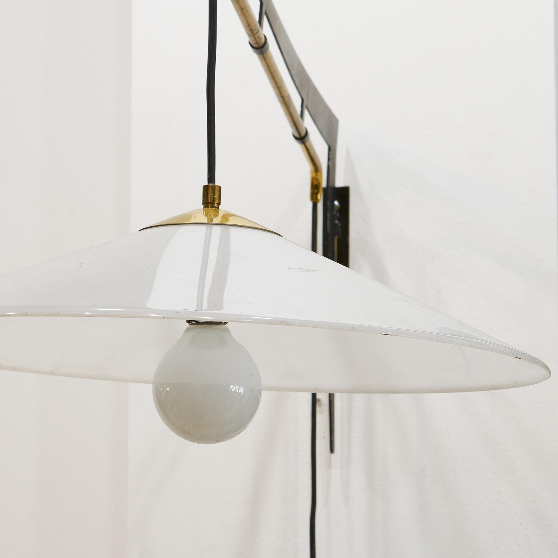 An Italian swing arm wall light designed by Stilux featuring a brass counterweight and adjustable height and projection features. The black metal frame mounts to the wall; utilizes one bulb. This has been newly rewired for US use. The shade is