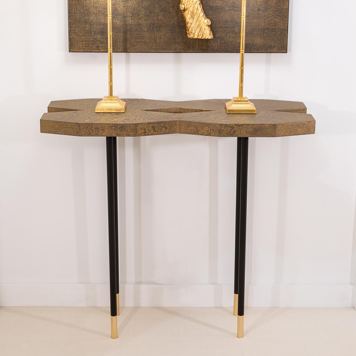 A sleek and sophisticated design of iconic contemporary aesthetic, this console features a striking X-shaped wooden top finished with gauze and an antiquated gold leaf coating, matching the shiny 18K gold-plated brass feet and in elegant contrast