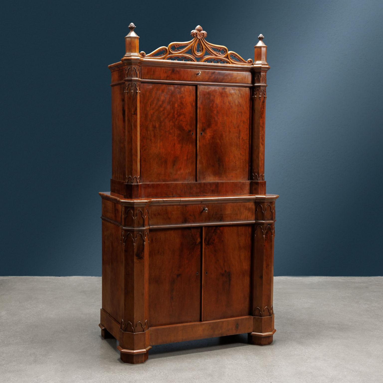Two-body cabinet completely veneered in mahogany feather; it has both in the narrower upper part and in the lower part two doors surmounted by a drawer and framed by a pair of uprights with an octagonal base. 

The mullions are embellished with