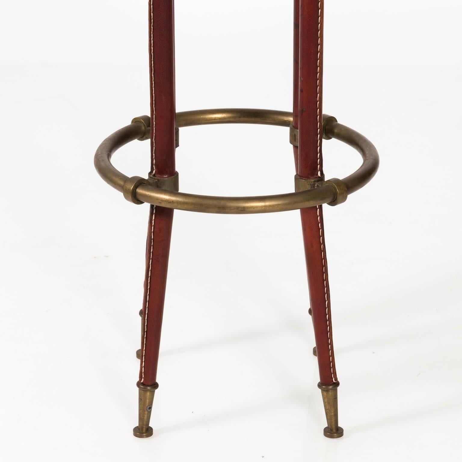 Pair of brass bar stools in stitched leather with circular leather seating, foot rests, and capped feet, circa 1955.
 