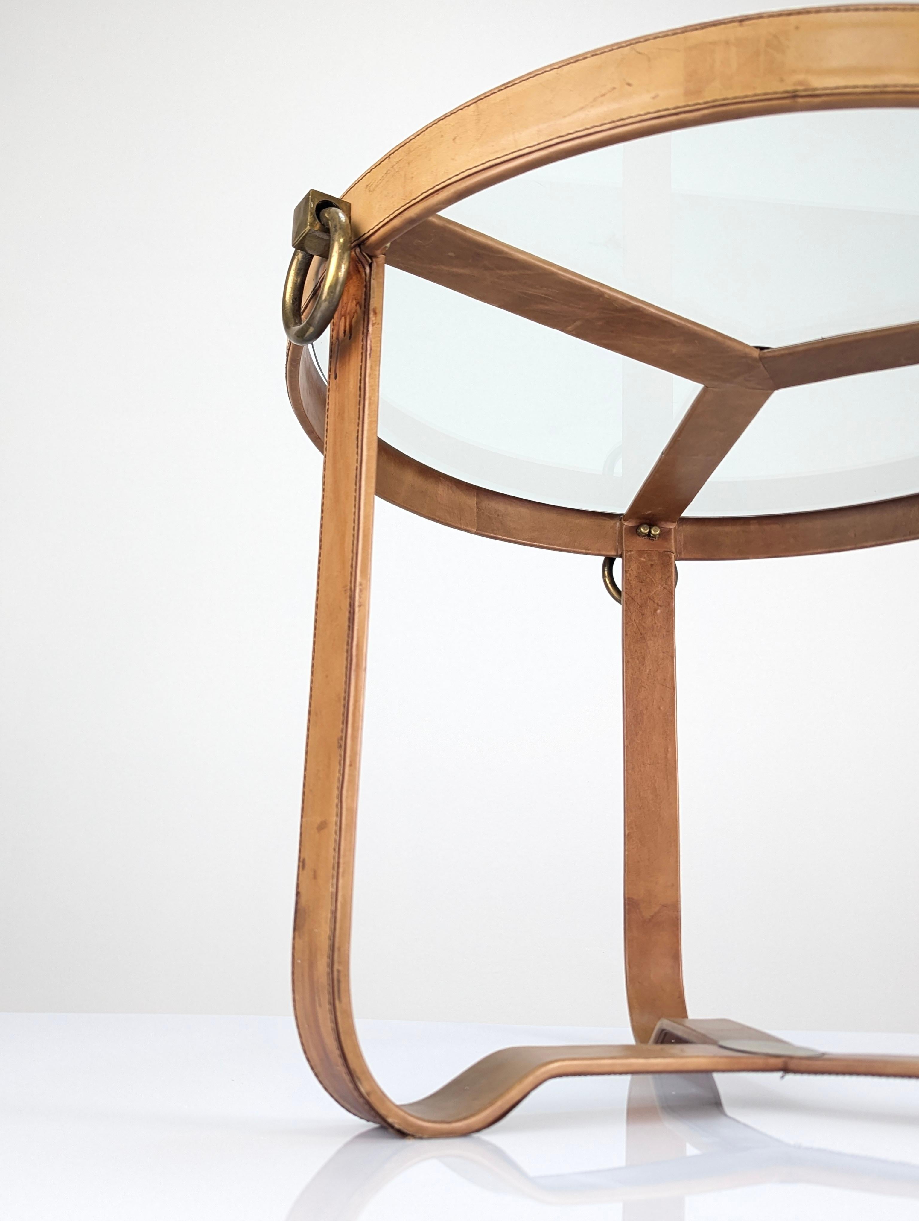 Table basse en cuir surpiqué et accents en laiton, inspirée des designs de Jacques Adnet des années 1970. Les designs intemporels et élégants d'Eleg sont toujours un succès décoratif dans n'importe quel espace. Cette table présente une silhouette