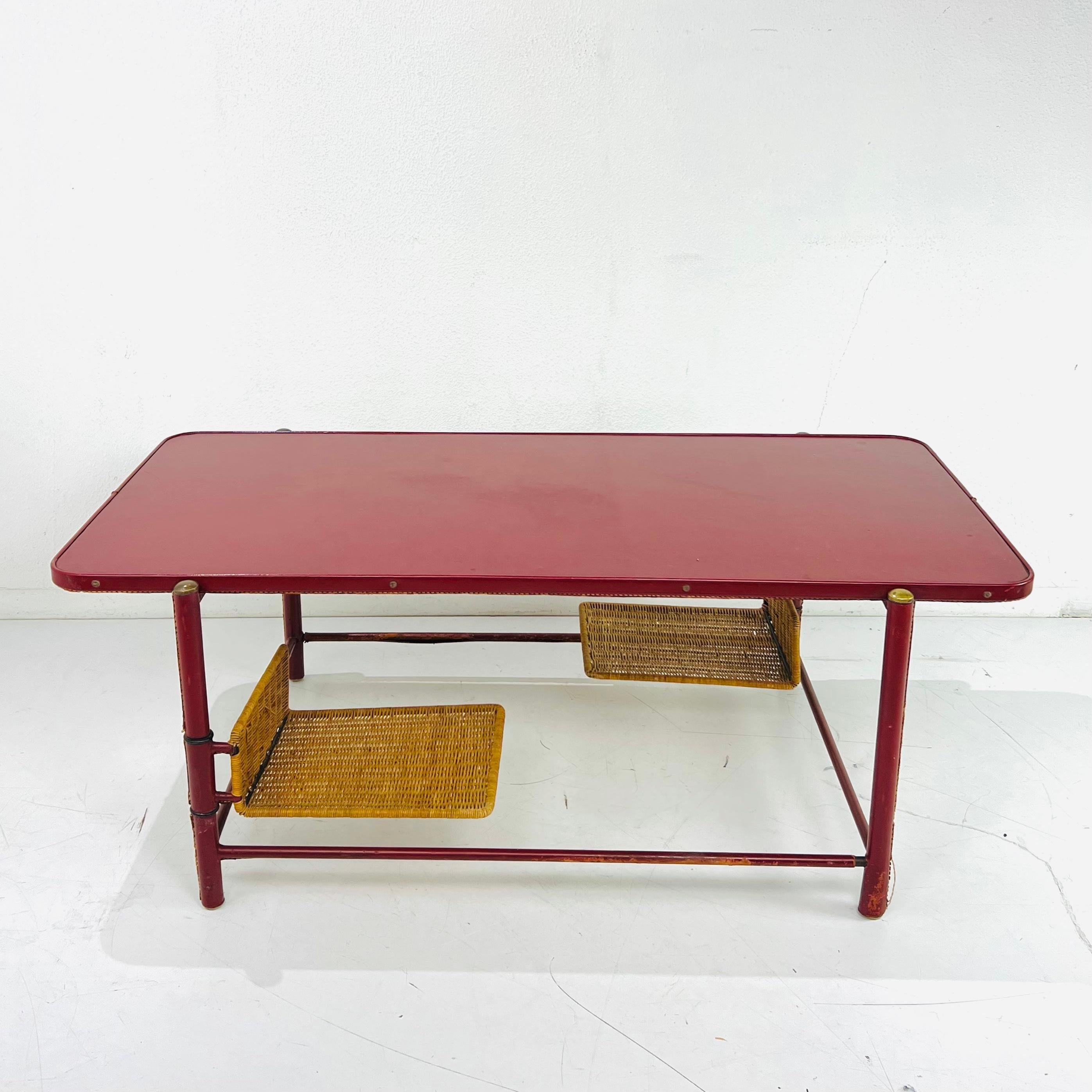 Je suis amoureux! Extraordinary vintage stitched leather coffee table in the style of Jacques Adnet. Wood and iron frame wrapped in hand-stitched red leather. Attached to the faux bamboo legs are two woven swing arm magazine holders and a stretcher