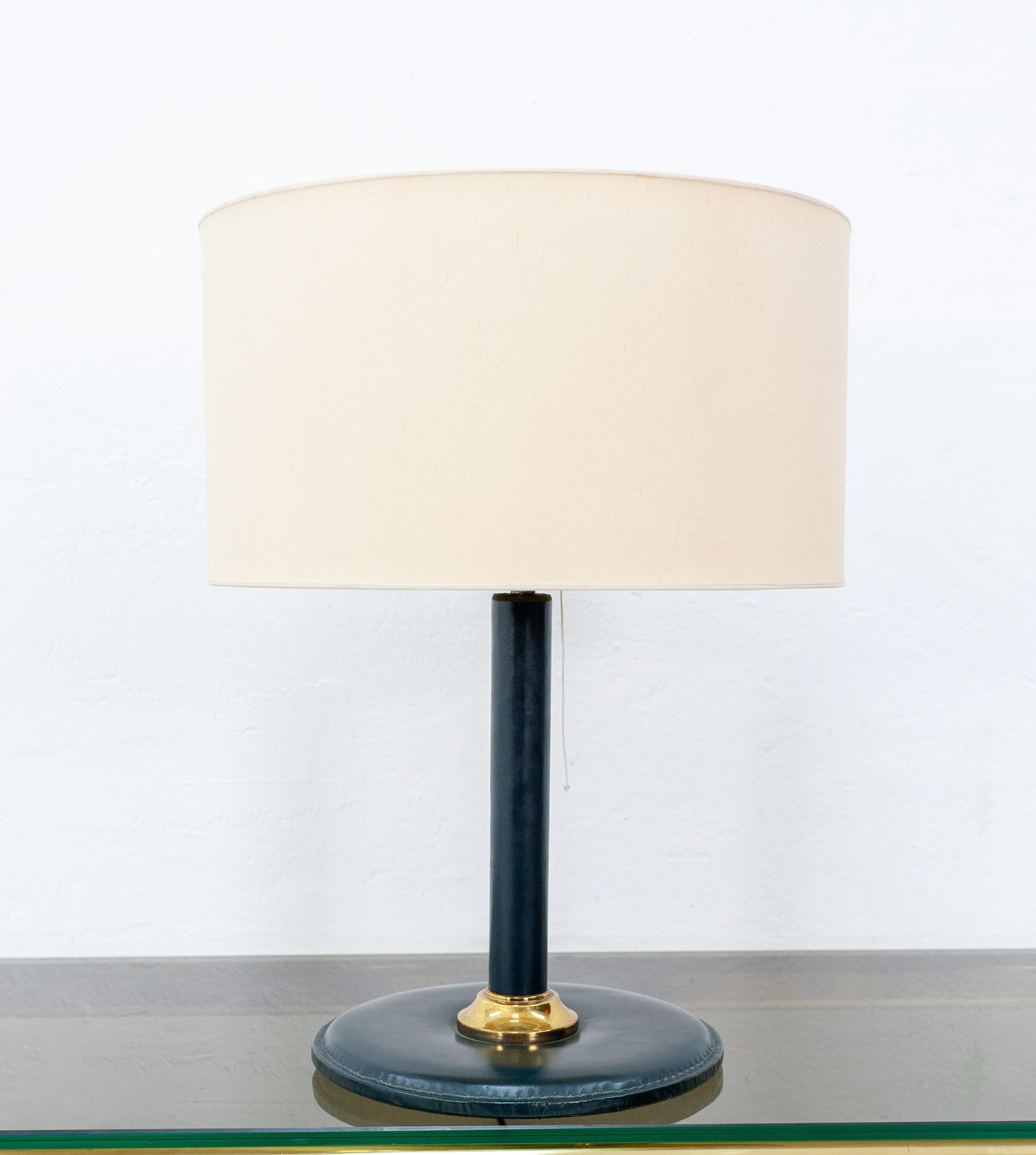 Beautiful forest green stitched leather table lamp. Attributed to Jacques Adnet. France 1960s. 
Still with its original closed top leather lampshade in a cream colored fabric. Recently rewired with a pull switch and a new armature.
There is some