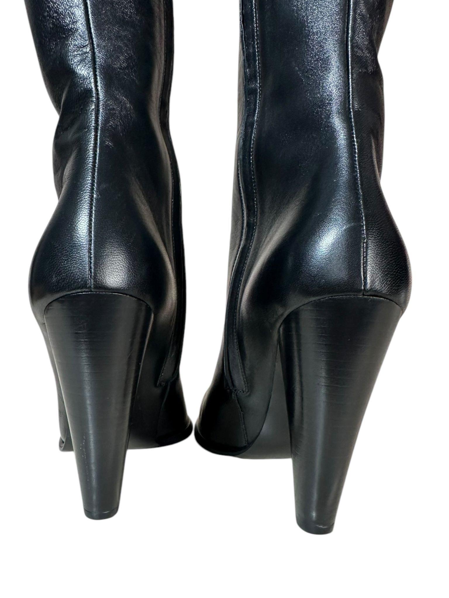 Bottes en cuir Tom Ford 
Matière : Fabriqués en cuir noir lisse et souple, ils offrent une finition brillante qui exprime la qualité et le luxe.
Design : Une botte à hauteur du genou avec une silhouette effilée qui met en valeur la ligne de la