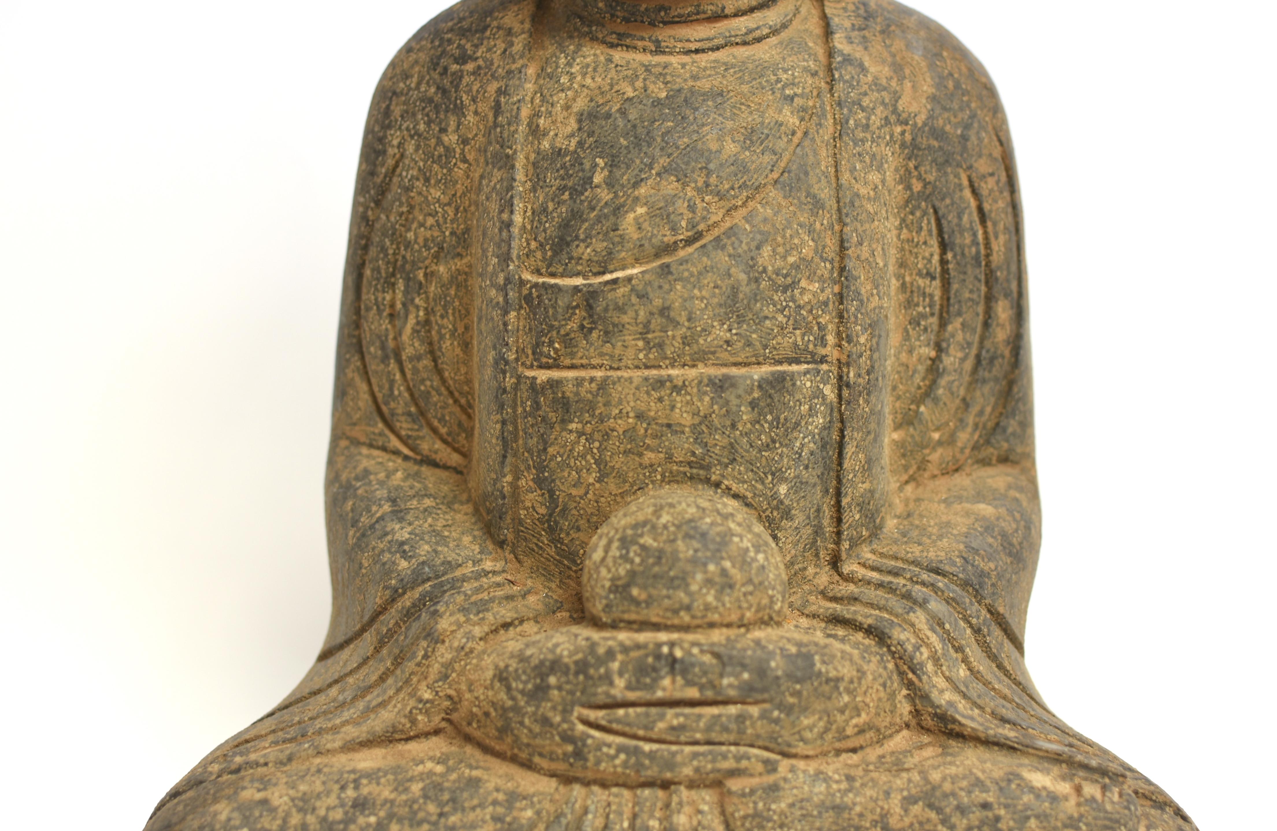 A beautiful solid stone statue of Buddha Amitabha. The face broad in Tang dynasty style, with downcast eyes and long earlobes, neatly coiled hair mounted on top of his head. Seated dhyana asana with hands in dhyana mudra, wearing a fluid robe folded