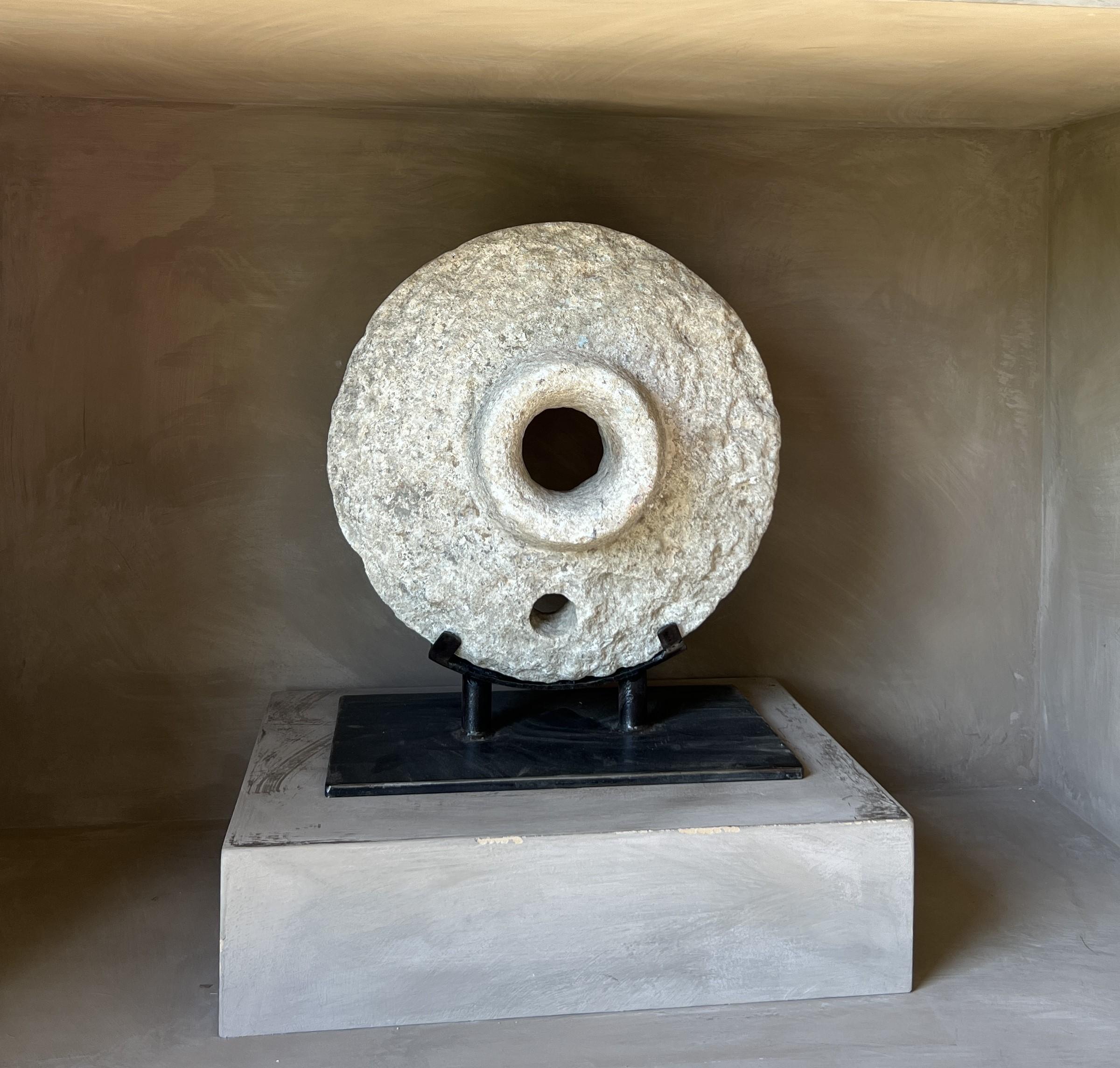 Interesting circular stone object. Most probably the lid of a stone mortar as examples found in south east Asia. 
Mounted on a custom stand it has its own sculptural quality. Combined with a beautiful color and patina it has a positive attractive