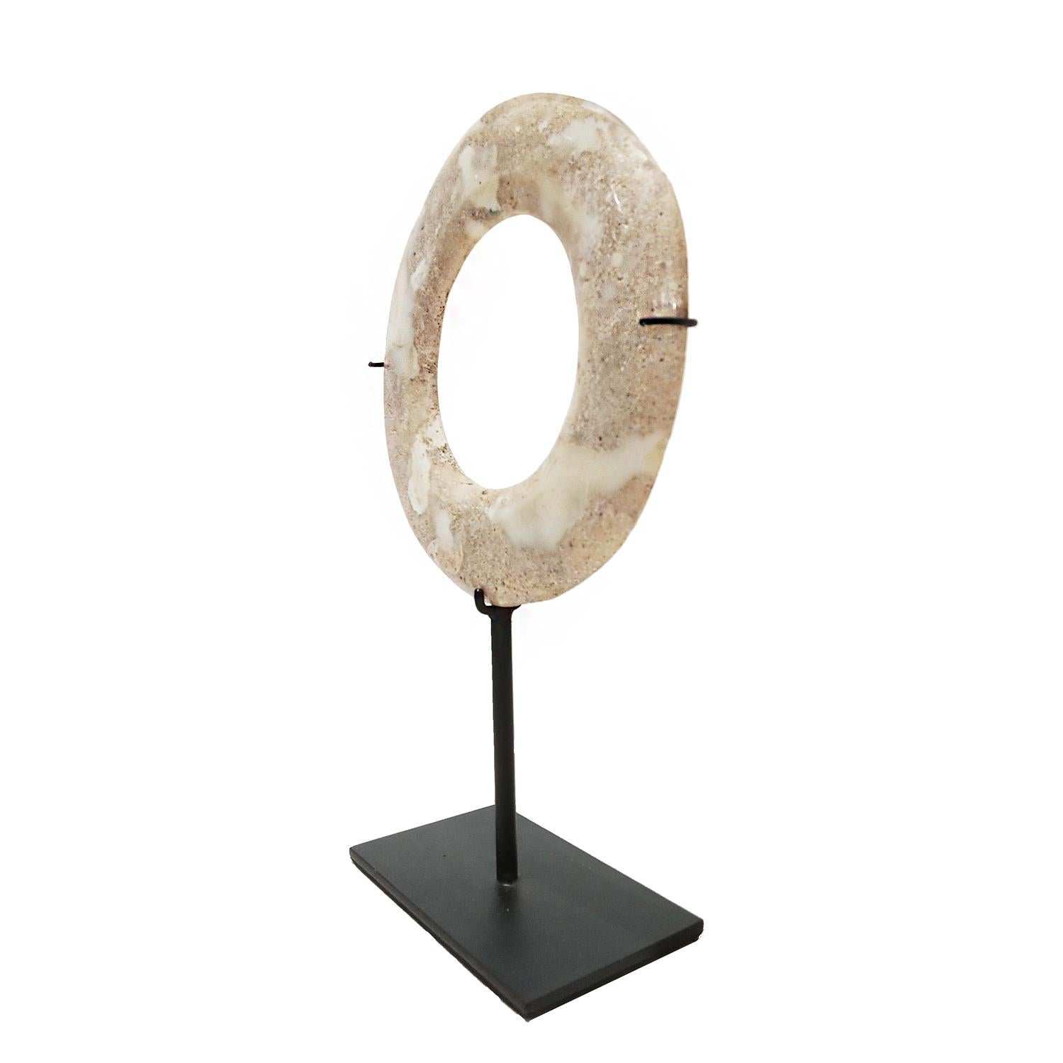 A beautiful stone disk, hand-carved in Indonesia. Mounted on a black metal stand. White stone, polished and shaped to resemble marble.

7.5 inches diameter, 2.75 inches deep (stand base), 11.5 inches total height (mounted). 

Other stone disks are