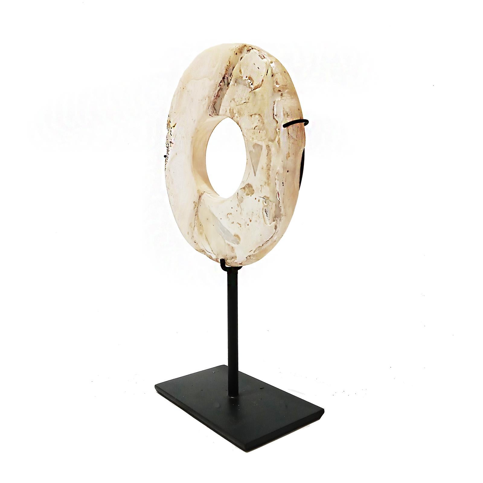 A beautiful stone disk, hand-carved in Indonesia. Mounted on a black metal stand. Cream-colored stone, polished to resemble marble and shaped into a disk.

7 inches diameter, 2.75 inches deep (stand base), 10 inches total height (mounted). 

Other