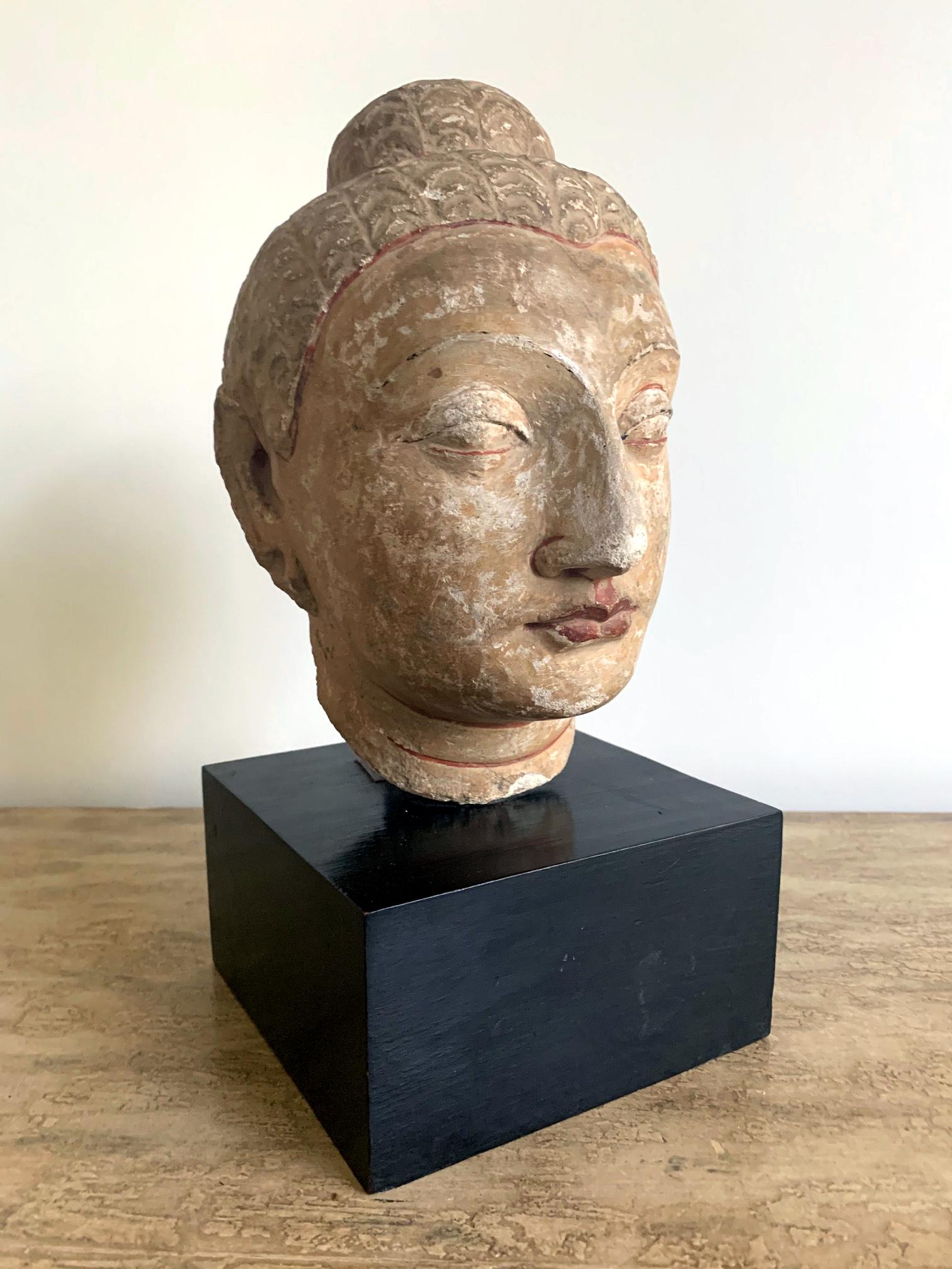 A carved and polychromed stucco on stone or possibly fired clay Buddha head of Gandahara style, a fragment from a larger statue mounted on a display stand, circa 2th-4th century. Gandhara is the name given to an ancient region or province invaded by