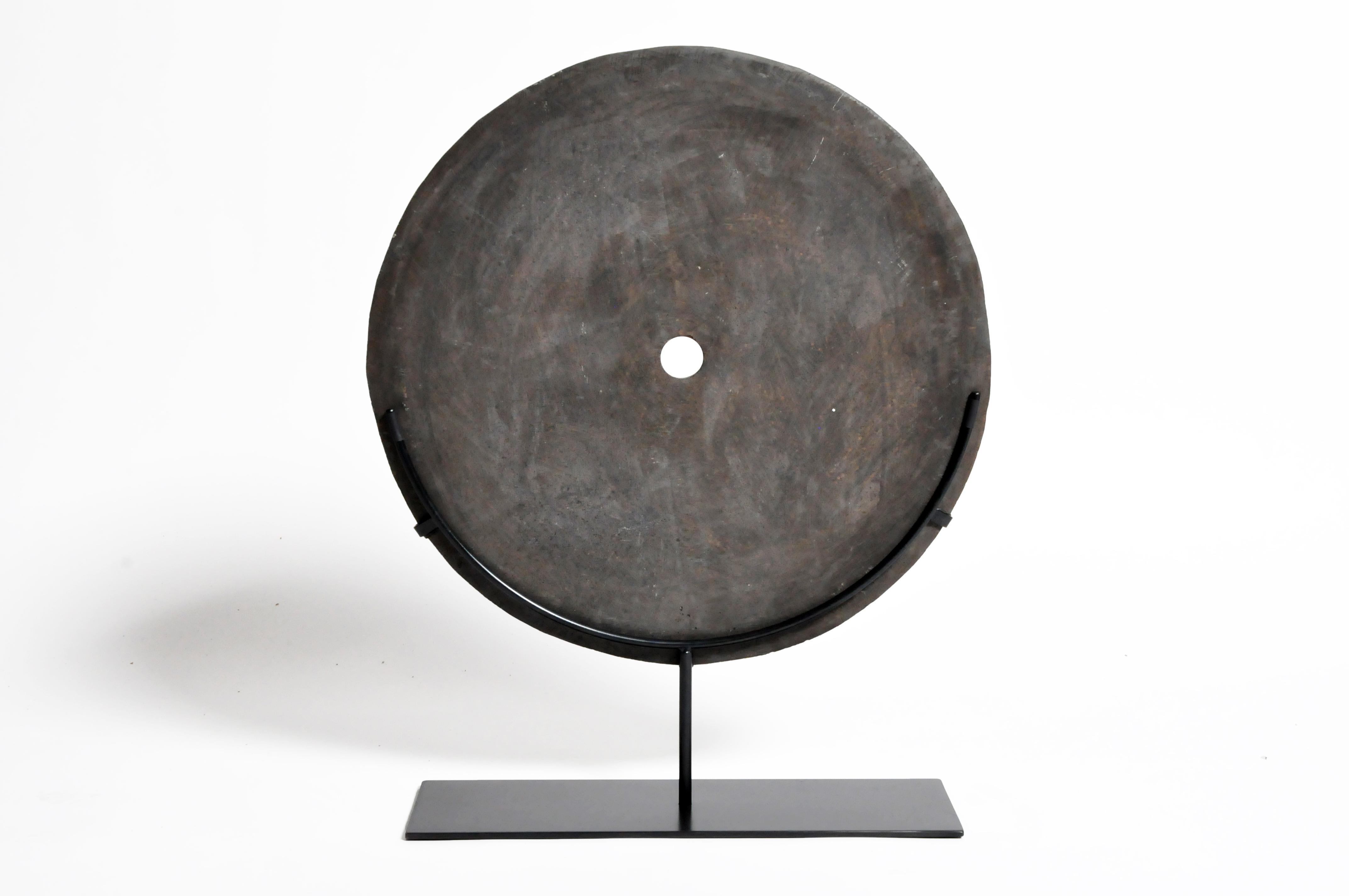 This stone grinding disk is from Timor and was made from basalt stone, circa 20th century. It is been mounted on a metal stand for display.