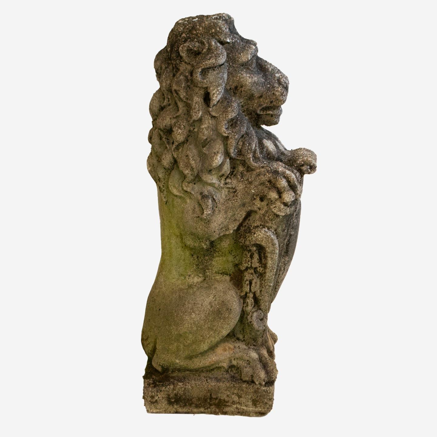 A pair of French carved cast stone lion garden statues from the 20th century, attributed to Antonio de Simone. These scrolled shield bearing lions are cast in a sitting position, with head facing forward with long, wavy mane and tail curled along