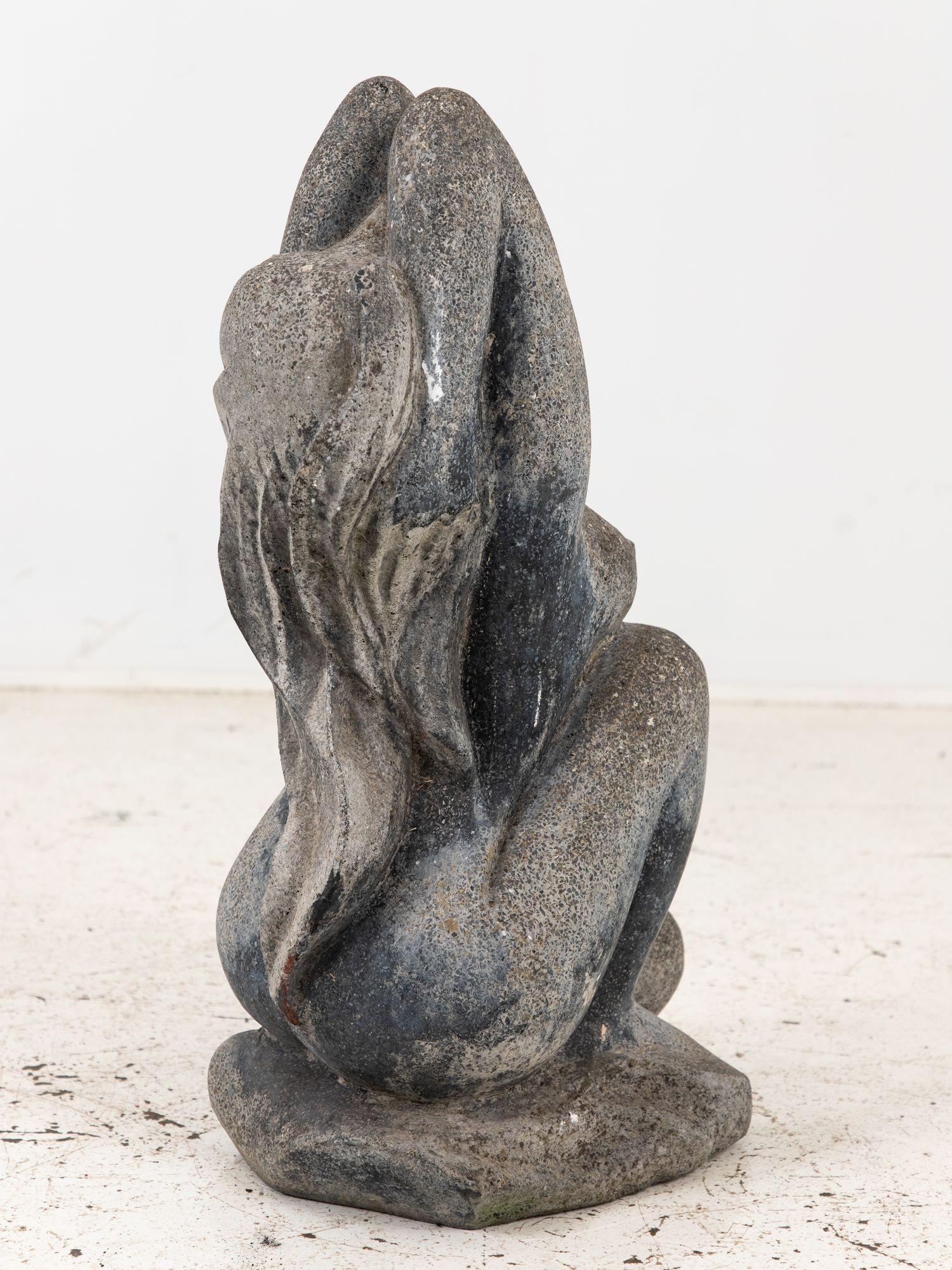 Carved from stone with masterful skill, this 20th-century sculpture portrays a woman in a moment of serene relaxation. With long flowing hair cascading down her back, she kneels gracefully, her posture exuding a sense of quiet strength and