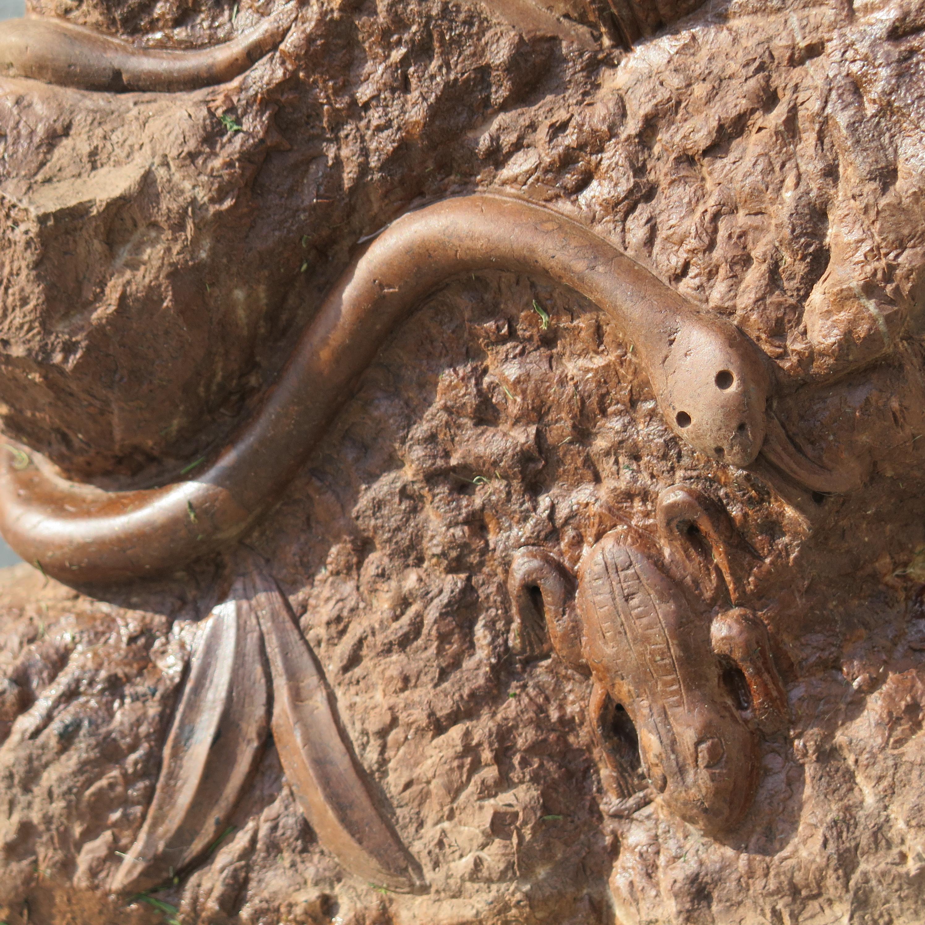 Carved in deep relief on stone is an undulating snake approaching a frog. There are smooth carved leaves as well on the textured stone carved by an unknown folk artist.