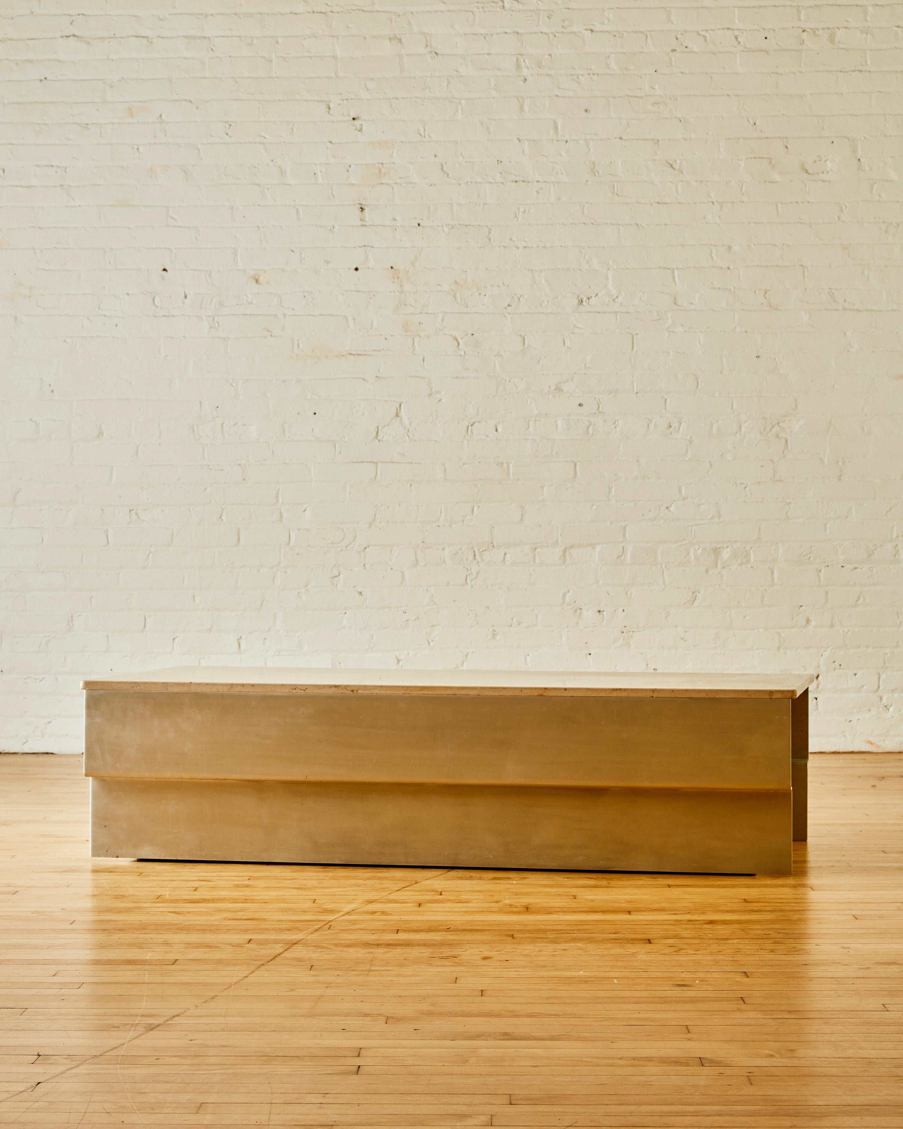 Table basse à plateau en pierre d'Ilan Dei Studio avec une base géométrique en métal brossé.

