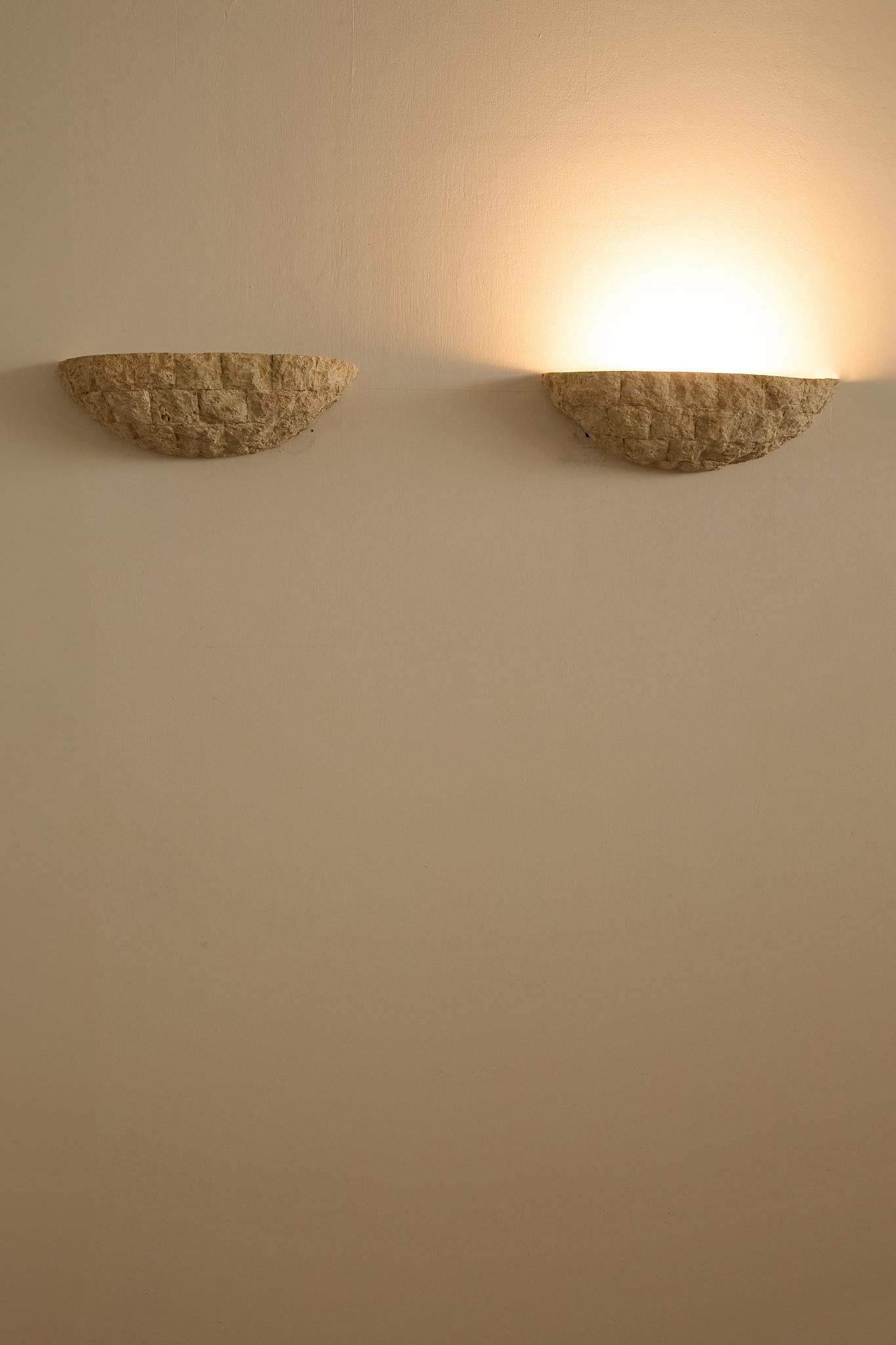 Handcrafted in textured stone, these sculptural half-moon sconces cast a warm, indirect glow. Their organic, rough-hewn surface evokes the character of traditional French masonry, while the simple geometric form gives them a timeless, architectural