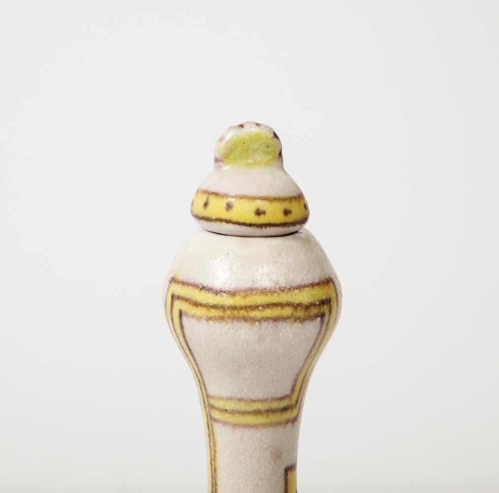 Stoneware. Bottle and stopper decorated with beige background. Yellow and brown interlocking motif throughout. Similar bottle available with a green geometric pattern.