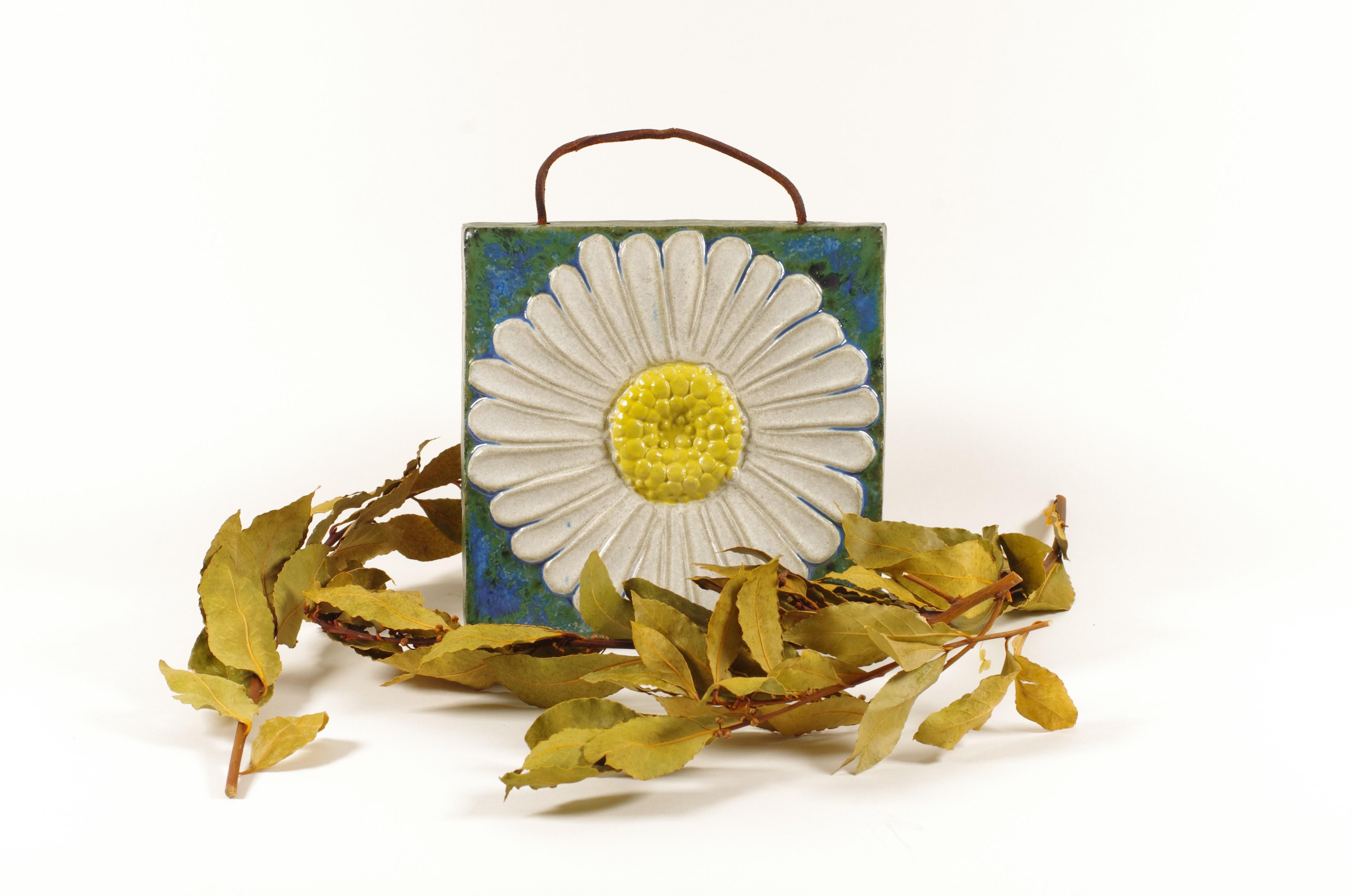 Targa decorativa da parete in gres di Willi Fischer, prodotta in Svezia negli anni Sessanta. Il rilievo raffigura un grande fiore di margherita in bianco e giallo su uno sfondo screziato di smalto verde e blu, che riflette la combinazione tipica di