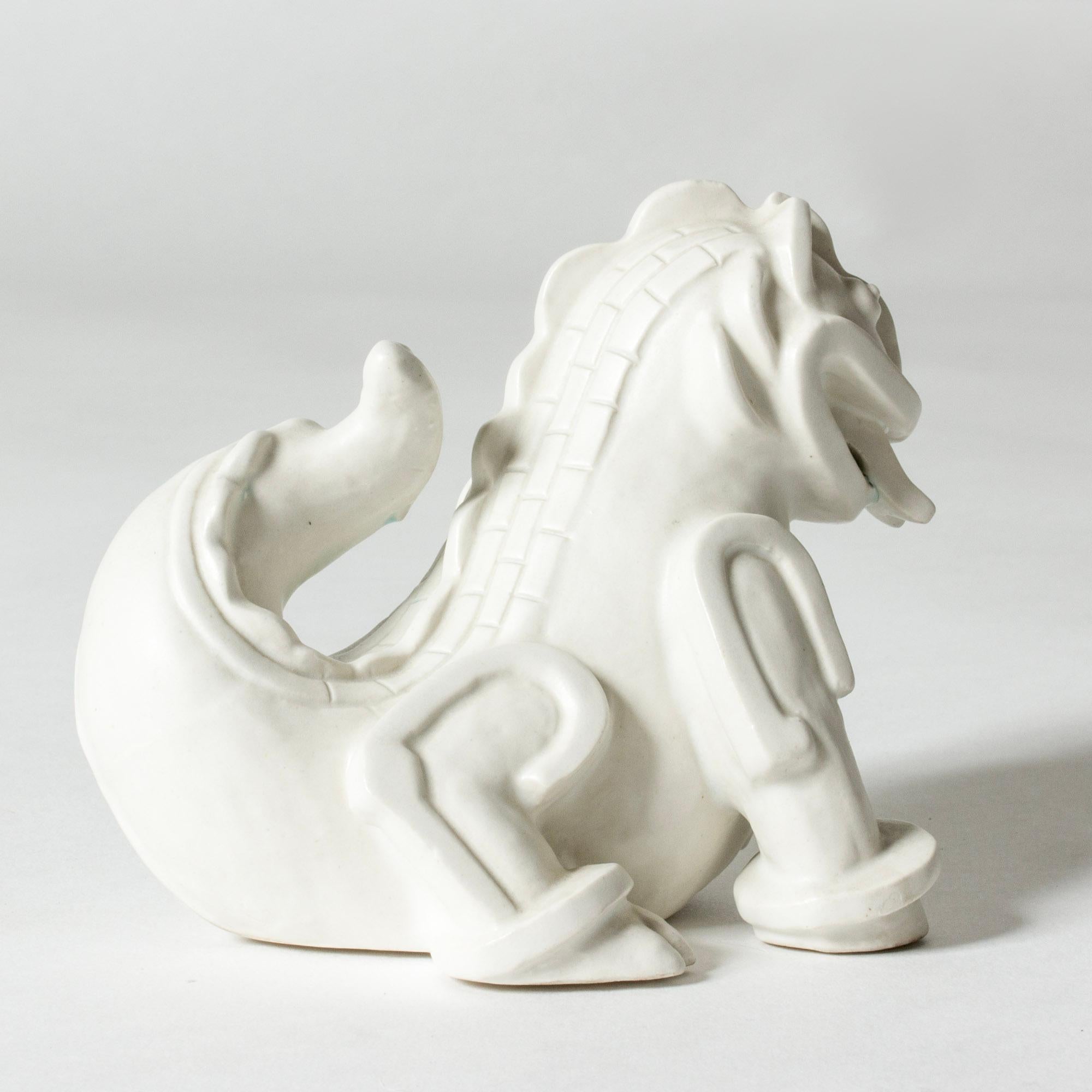 Adorable “Dragon Puppy” figurine by Wilhelm Kåge, made from stoneware with white cararra glaze. Fun and mischievous design, inspired by Chinese Ming era dragon sculptures and executed in Kåge’s distinct artistic style. . Stains of celadon green