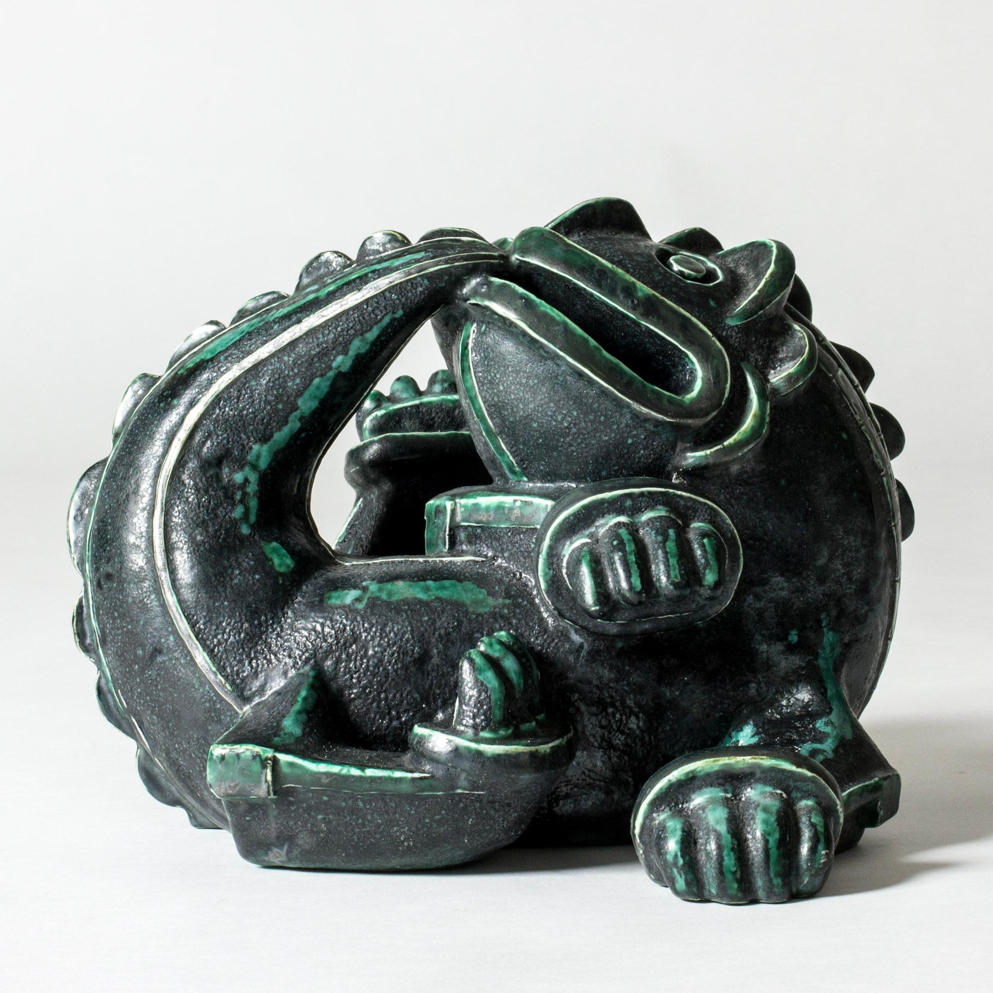 Amazing, unique dragon sculpture by Wilhelm Kåge, made from stoneware with deep green glaze with a grainy expression. Rare, large size. Lively design with a charming mischievous expression, inspired by Chinese Ming era dragon sculptures and executed