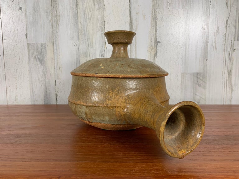 Ochre stoneware lidded bowl with massive handle.