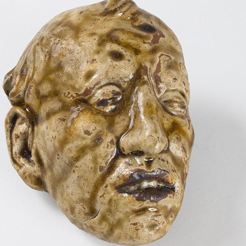 A French stoneware mortuary mask by Rupert Carabin. The mask is of a man's face. It is finished in beige and brown glaze. 

In the pursuit of a sophisticated anatomical knowledge, Rupert Carabin attended public dissections at the Paris faculty of