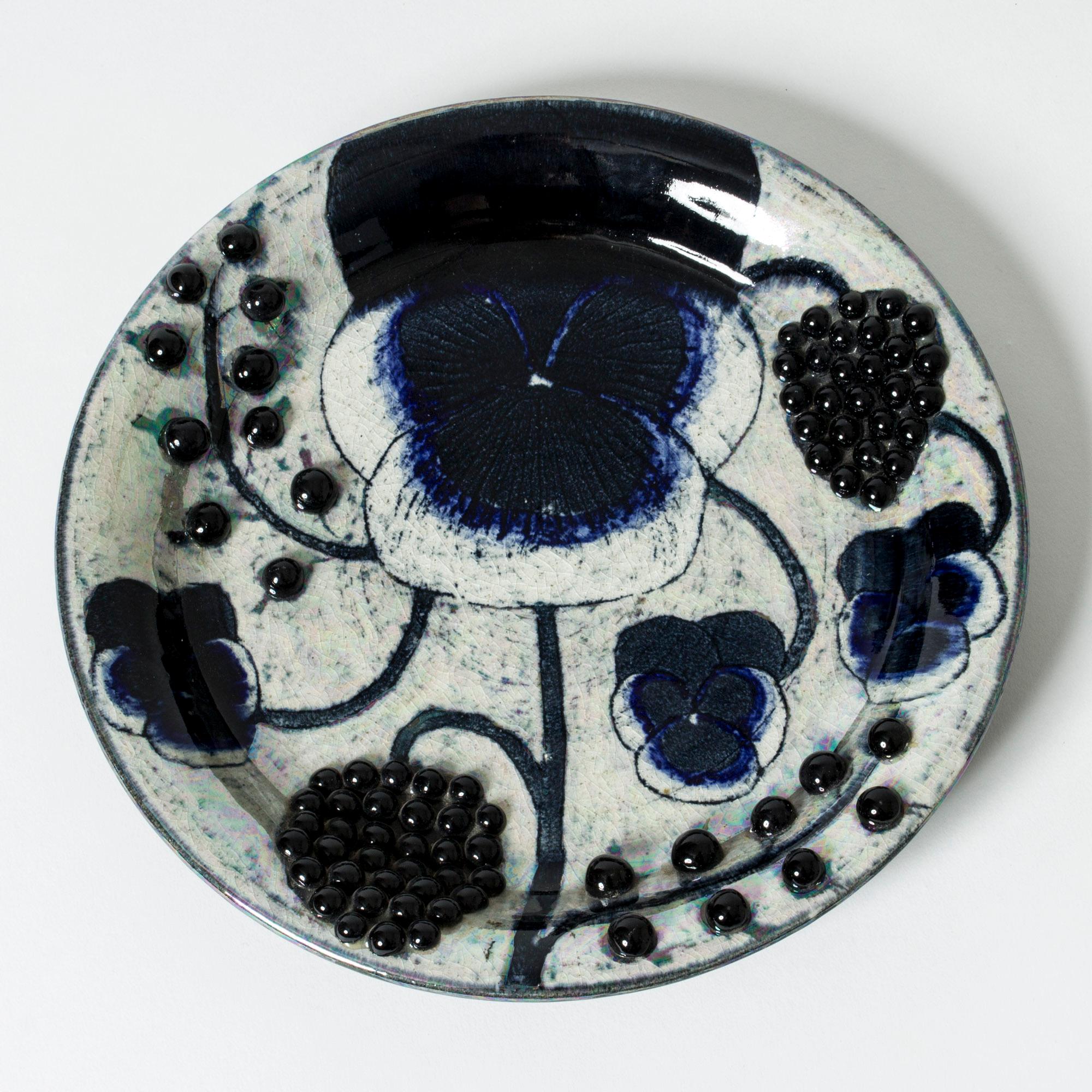 Beautiful, unique stoneware platter by Birger Kaipiainen in an oval form. Motif of a pale yellow poppy with black round seeds in relief, contrasting in a suggestive way against a dark background. Highlights of iridescent glaze.
