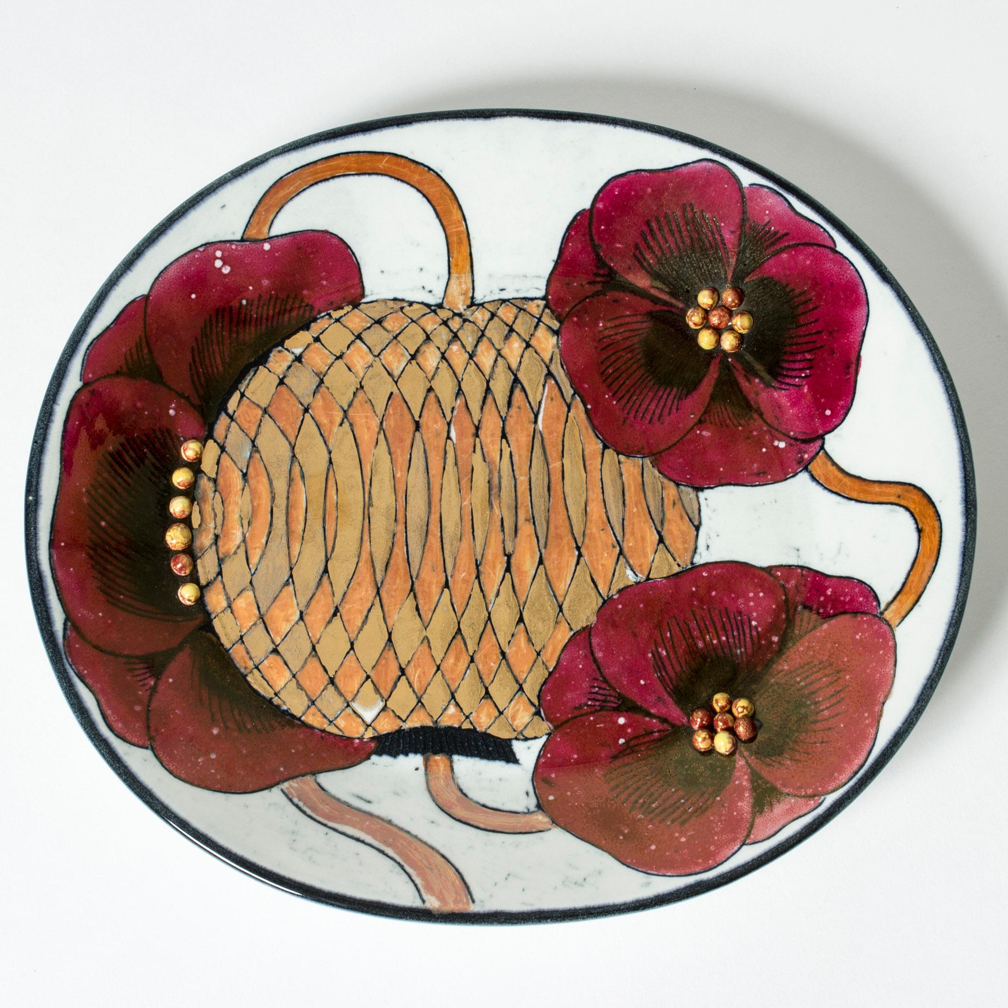 Unique stoneware platter by Birger Kaipiainen in an oval form. Striking motif of red flowers encircling a large seed pod with a graphic pattern in golden tones. Round seeds in the center of the flowers in relief.