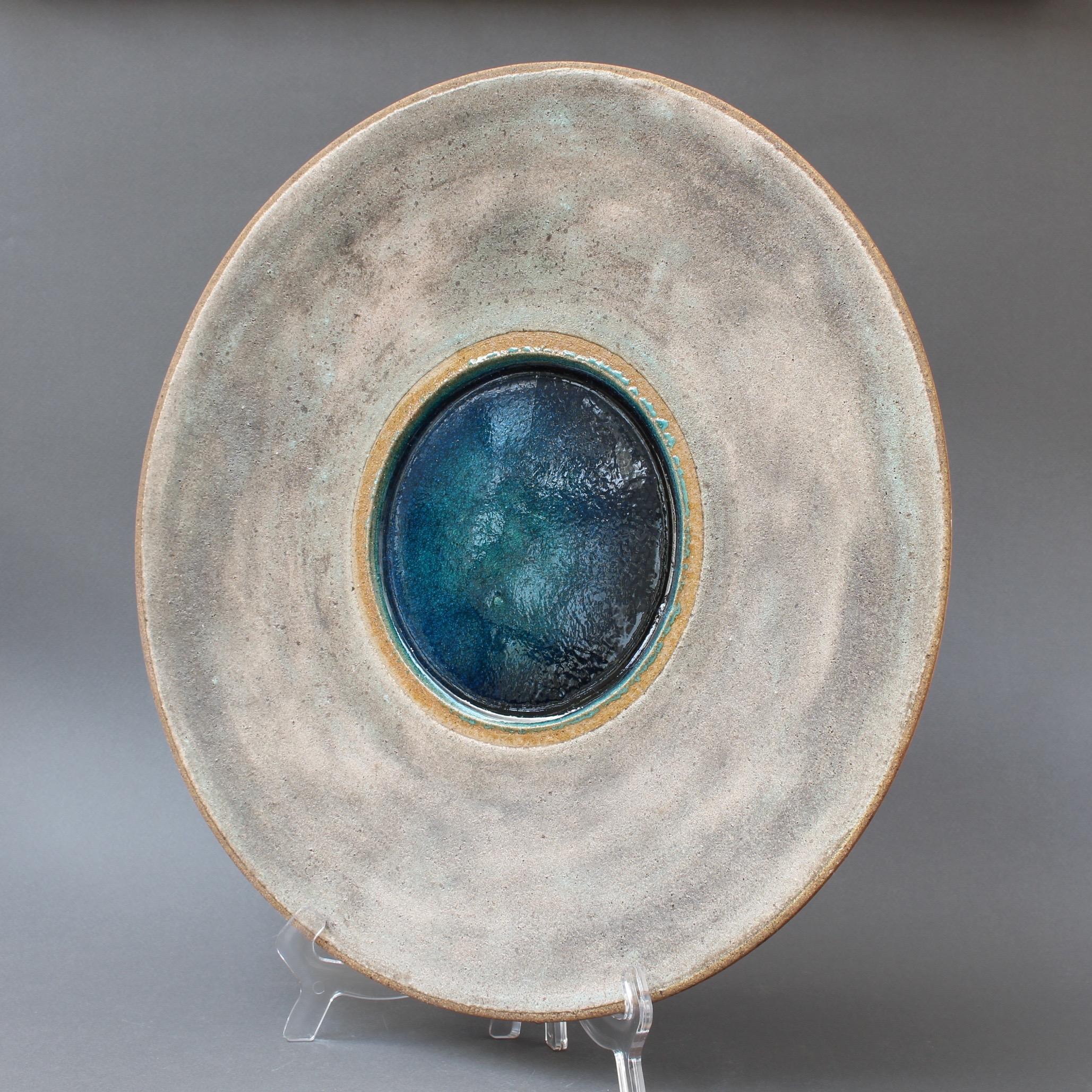 Large stoneware platter with molten glass centre by Bruno Gambone (circa 1980s). A natural stoneware finish in grey and beige with clay brown lip and centre-surround all complement the stunning molten deep blue glass focal point. A rare find from