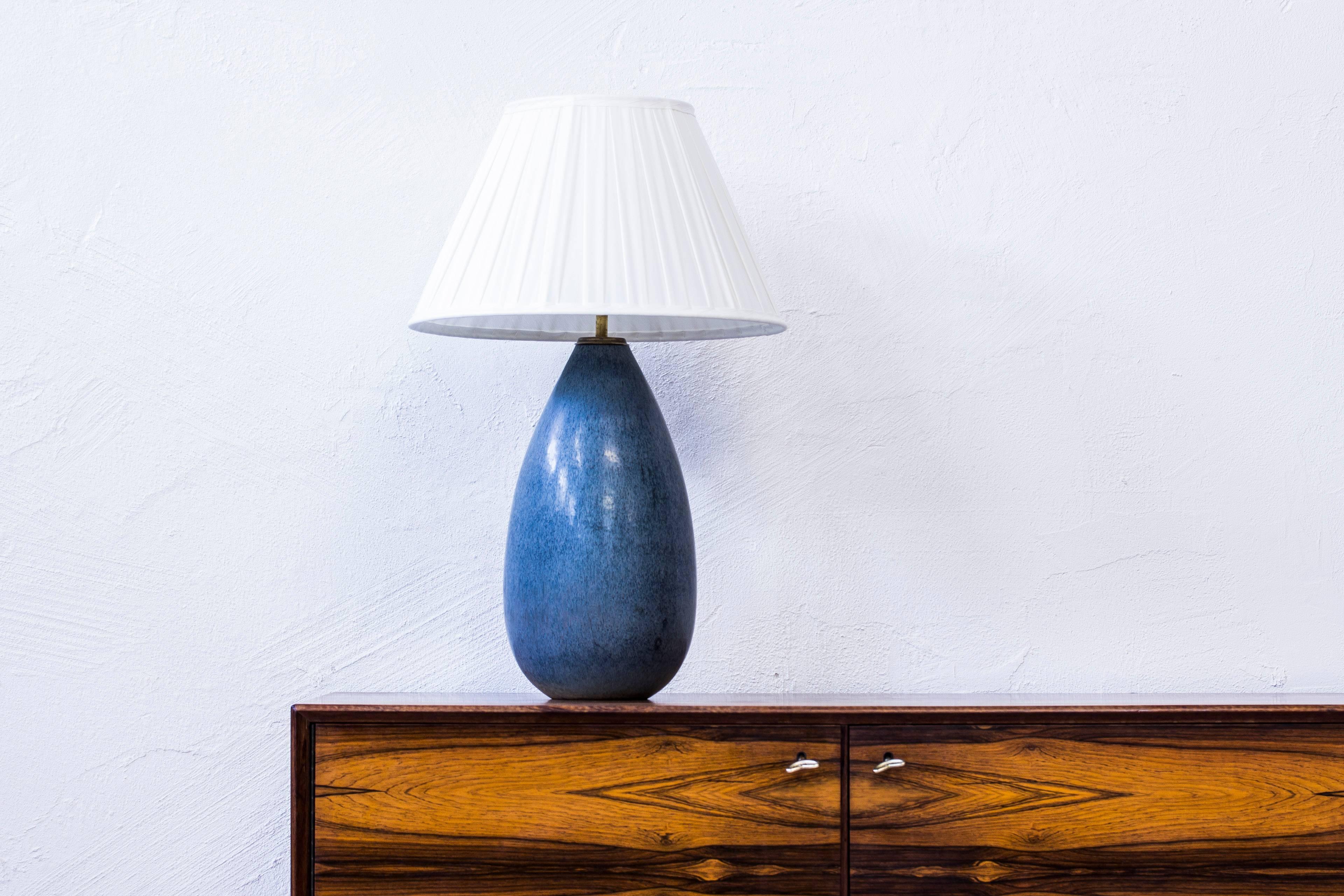 Table lamp designed by Carl Harry Stålhane. Produced by hand at Rörstrand during the 1950s. Blue, grey glaze with hints of purple. Brass fitting on the top. With new hand-sewn, pleated chintz lampshade. Excellent condition with light age related