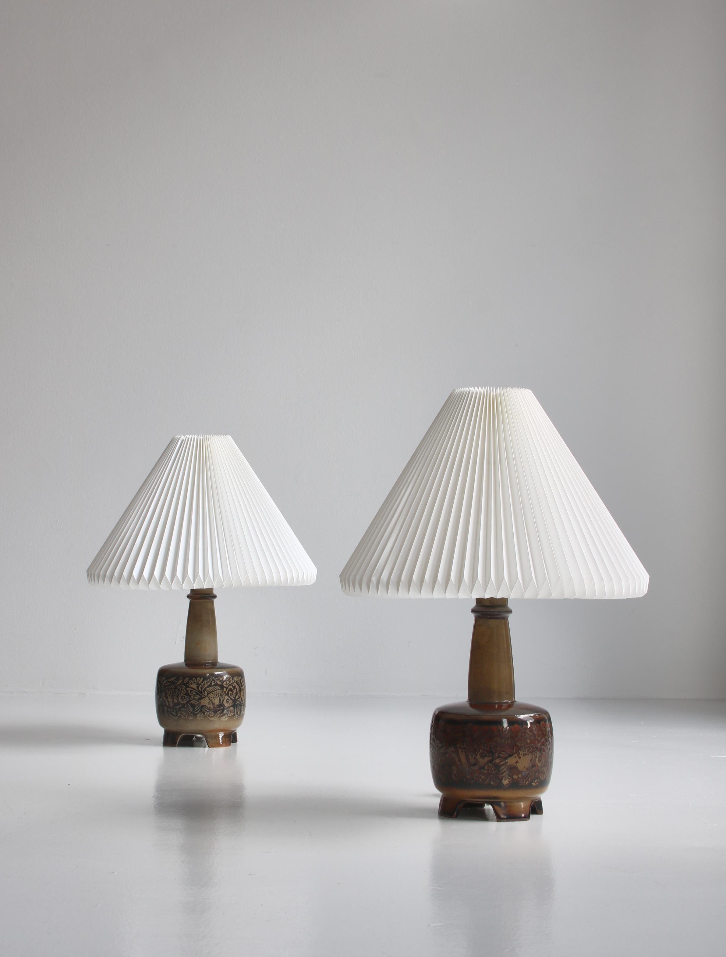 Wonderful pair of hand made ceramic table lamps made by Nils Thorsson for Royal Copenhagen in the 1950s. The table bases are decorated with fish motifs and a glazing in earth colors. Mounted with new white hand folded Le Klint shades. Rewired and