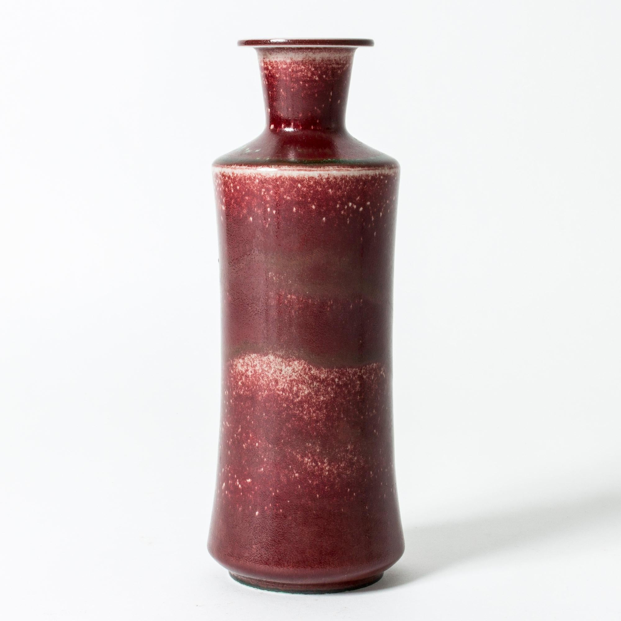 Large stoneware vase by Berndt Friberg in a tall design, with a deep and lustrous oxblood glaze, contrasted with jade colored streaks and unglazed speckles.

Berndt Friberg was a Swedish ceramicist, renowned for his stoneware vases and vessels for