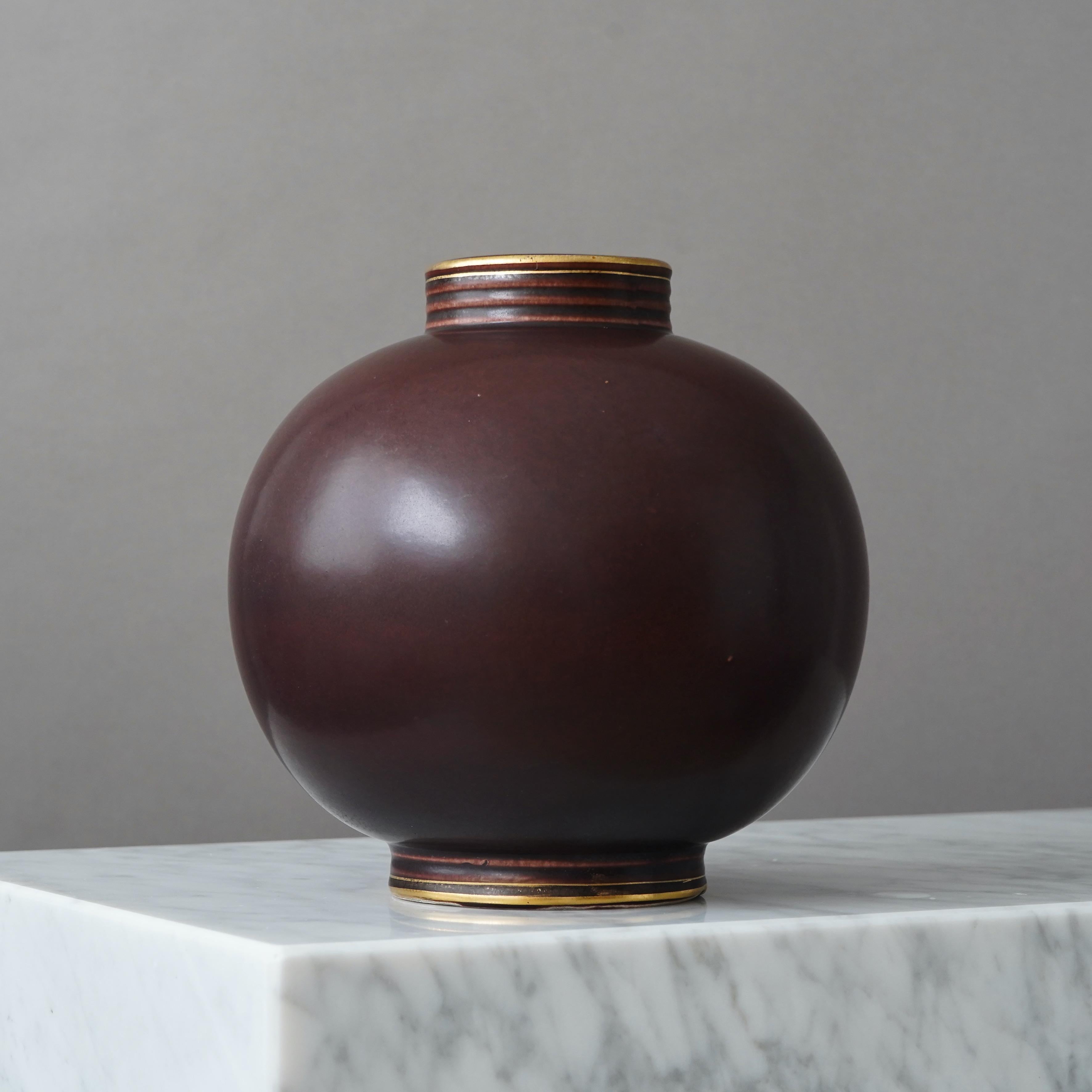 Un bellissimo vaso in gres con un'incredibile smaltatura e dettagli dorati dipinti a mano.
Disegnata da Gunnar Nylund per Rorstrand, Svezia, anni '1930.  

Buone condizioni. Prima la fabbrica. Un'ammaccatura sul bordo del piede dovuta alla