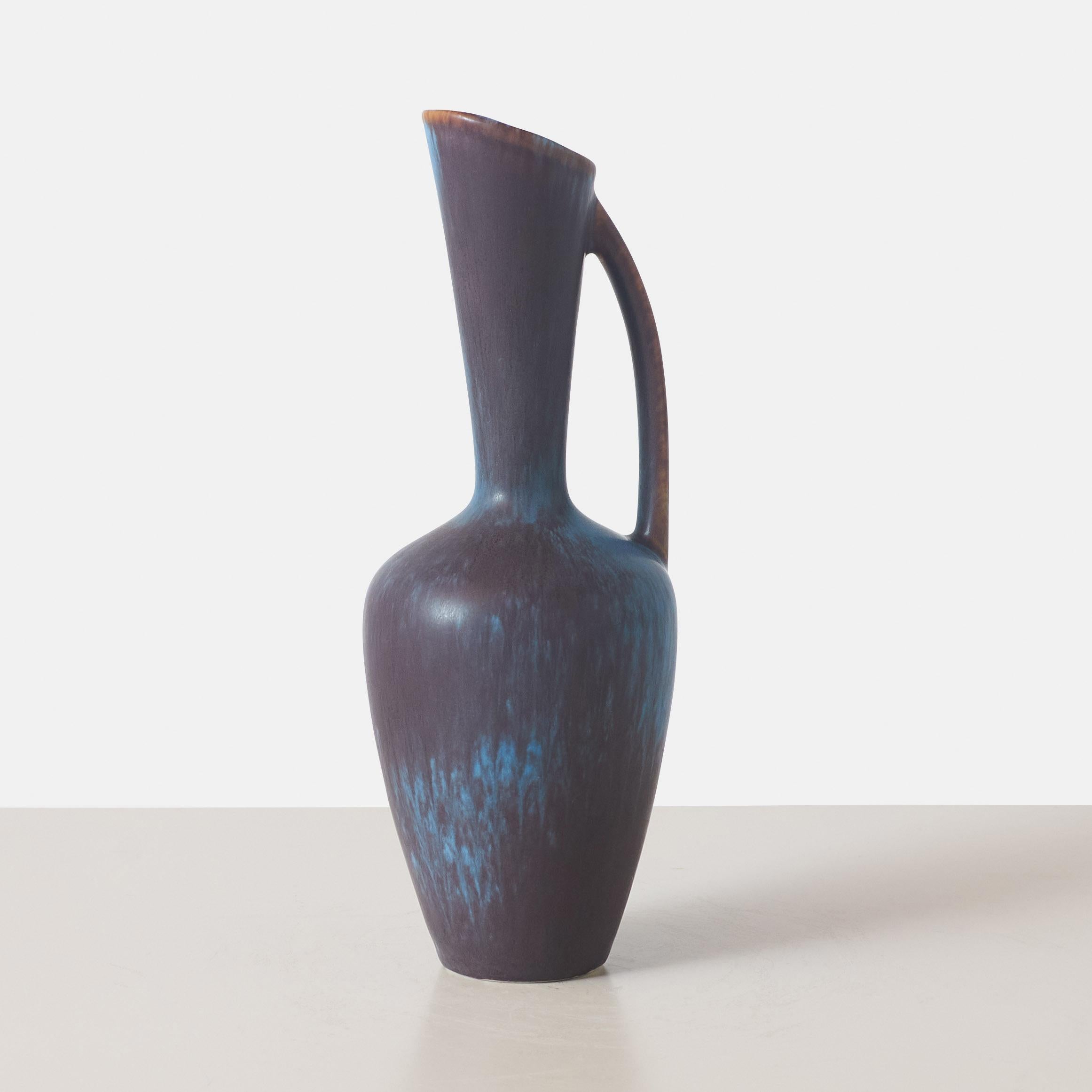 An elegant ceramic vase by Gunnar Nyland with a tall spouted neck and curved handle in shades of blue. Made for Rorstrand, inscribed with Rorstrand mark and GN AXQ.