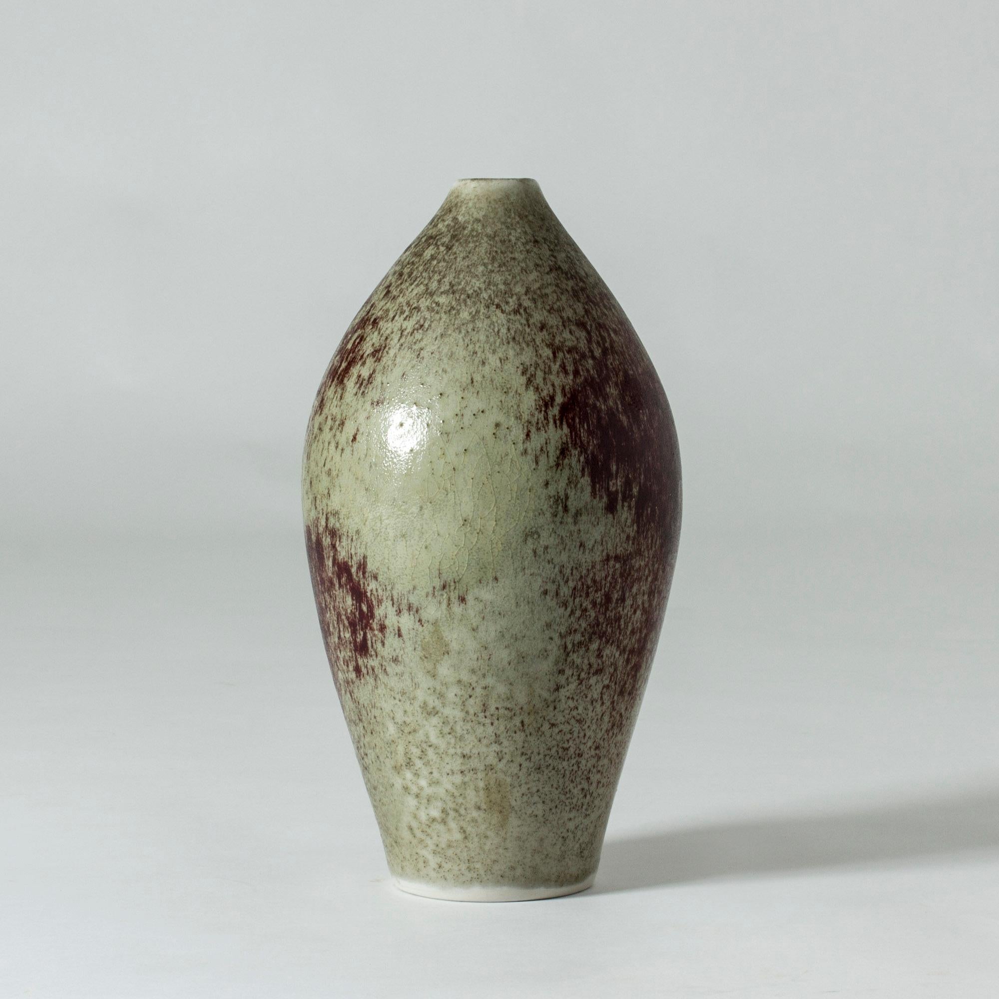 Beautiful stoneware vase by Toini Muona. Simple, oval shape with some structure on the surface. Sand colored and dark red oxblood glaze in dramatic splashes.