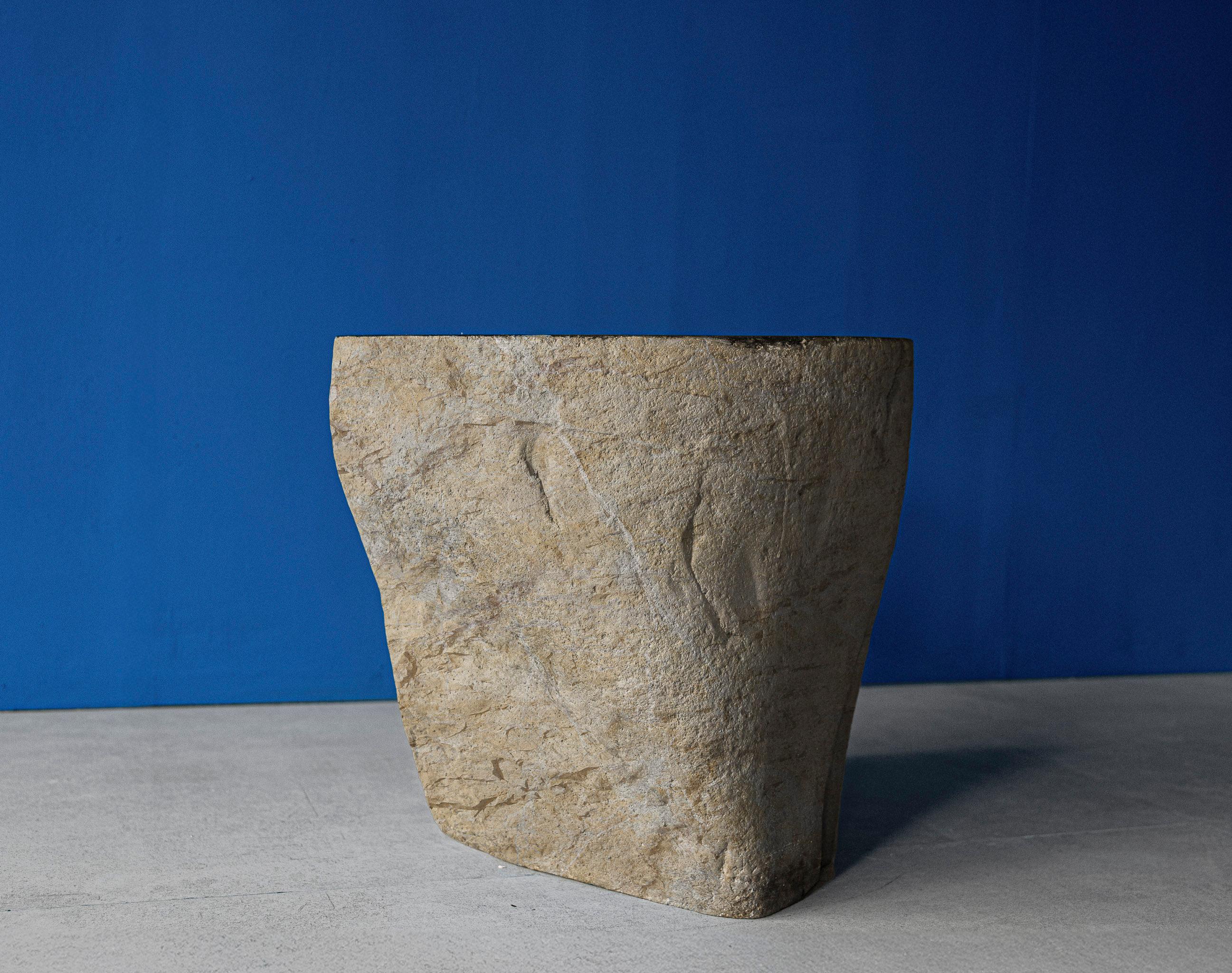 Le tabouret 77 est un tabouret polyvalent ou un meuble d'appoint sculpté dans de la pierre de rivière solide, mettant en valeur la beauté brute des matériaux naturels. Ses contours organiques et sa surface texturée en font un tabouret, une table