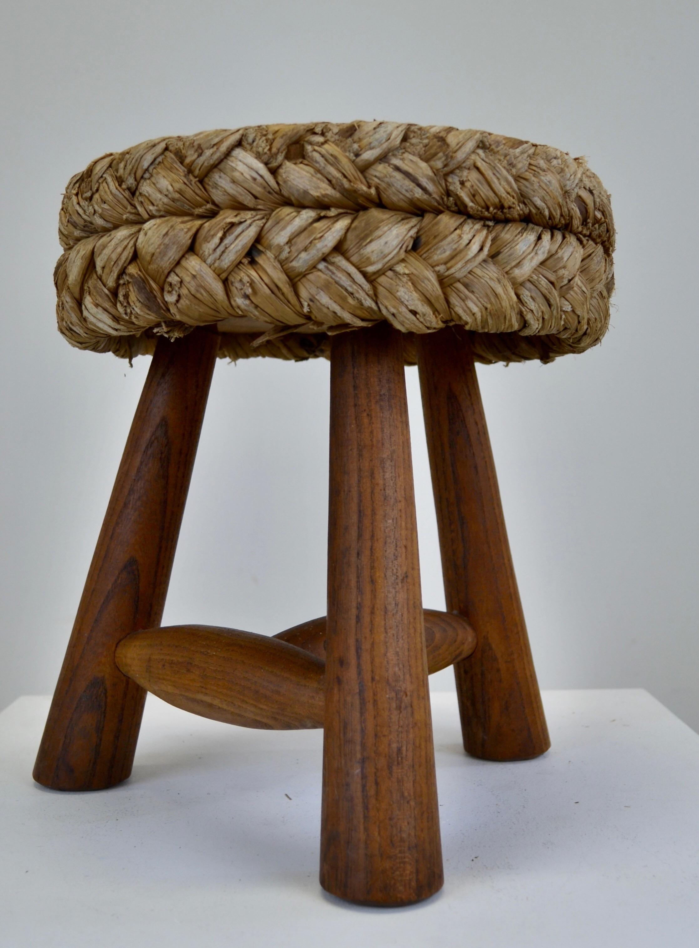 Mid-century French low Shepard's stool designed by Adrien Audoux and Frida Minet. This rustic French pouf showcases a circular seat crafted from woven raffia/rattan, supported by tripod legs and an oak keel base. Maintaining its original condition.
