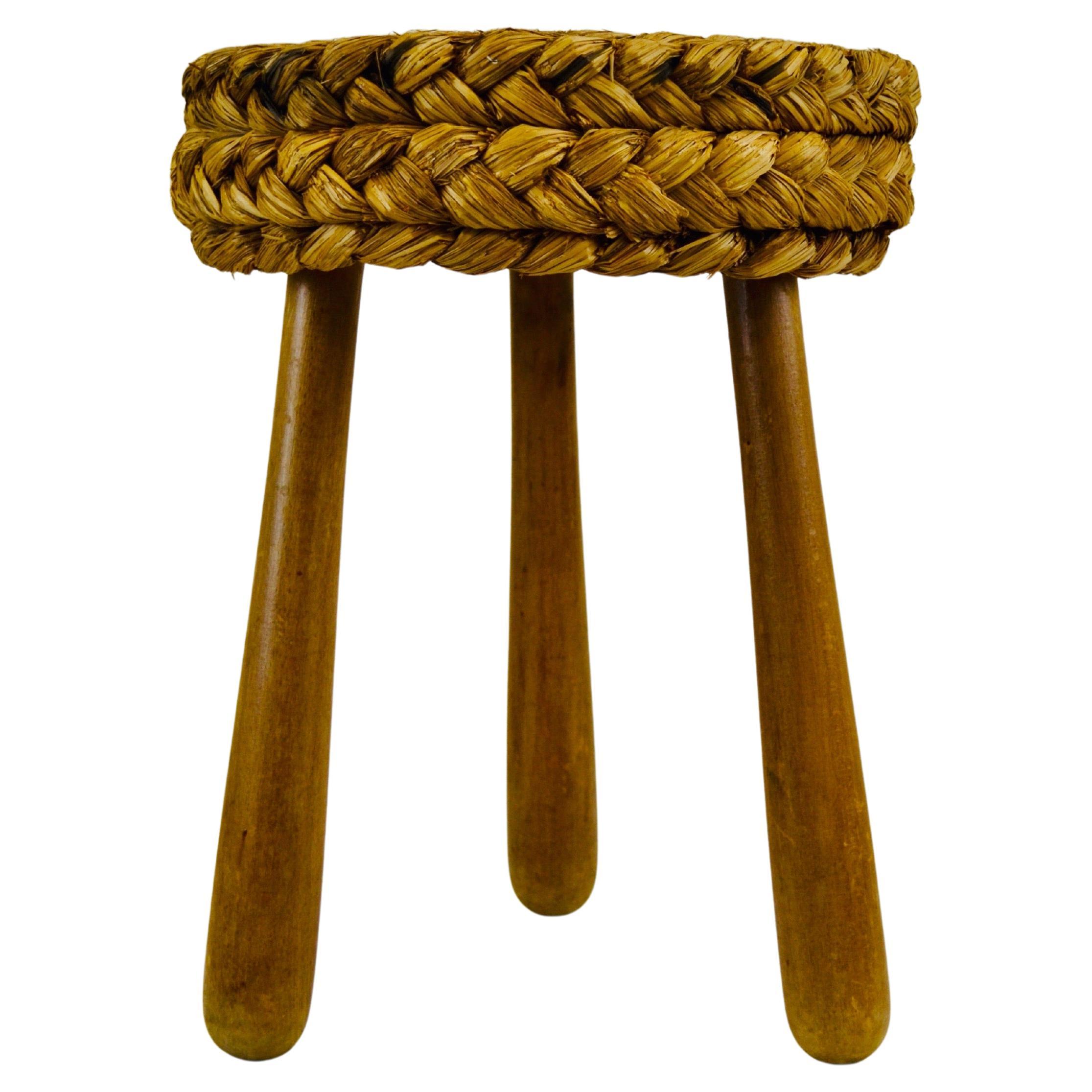Mid-century French low Shepard's stool designed by Adrien Audoux and Frida Minet. This rustic French pouf showcases a circular seat crafted from woven raffia/rattan, supported by tripod legs and an oak keel base. Maintaining its original condition.