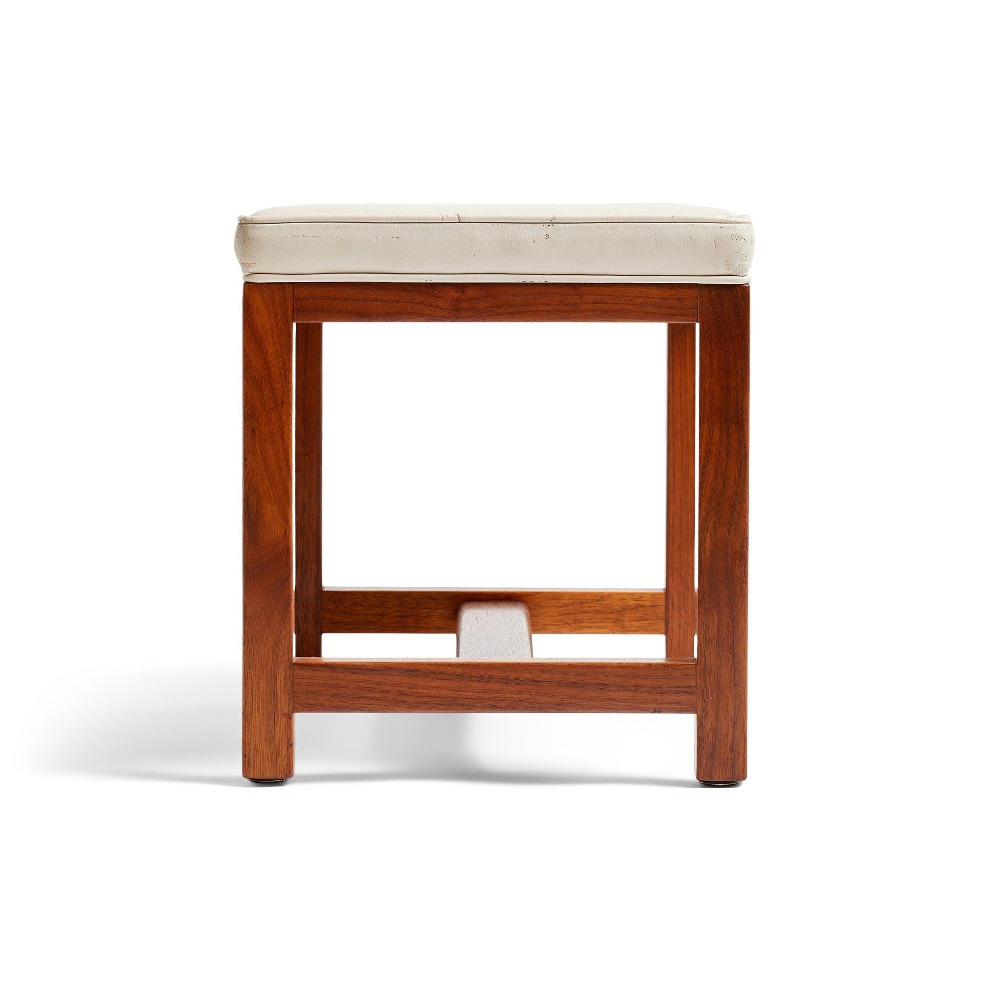 Ein rechteckiger Hocker mit Lederkissen auf einem massiven 